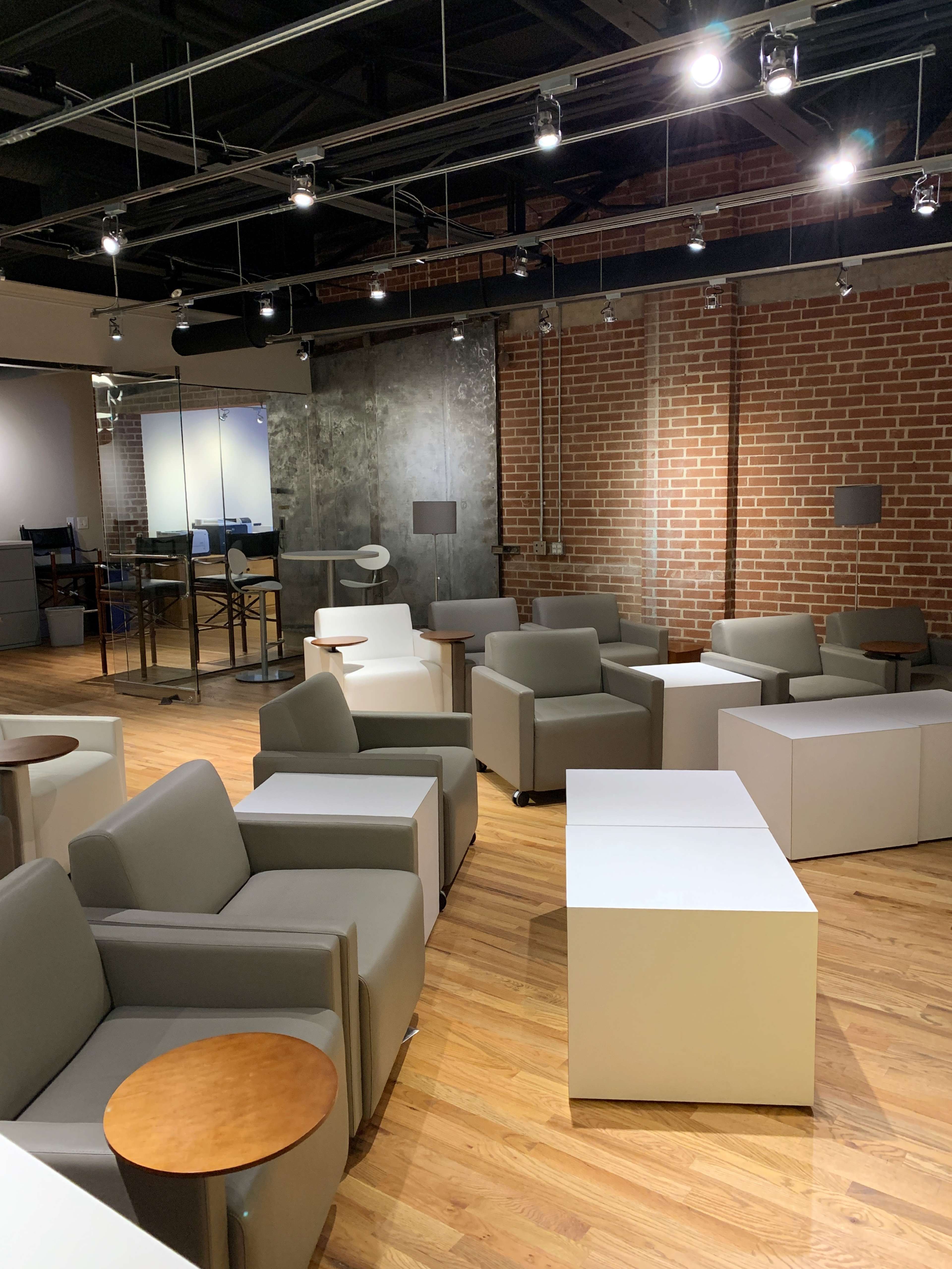 A modern lounge area with gray seating arrangements, wooden side tables, and a brick wall backdrop.