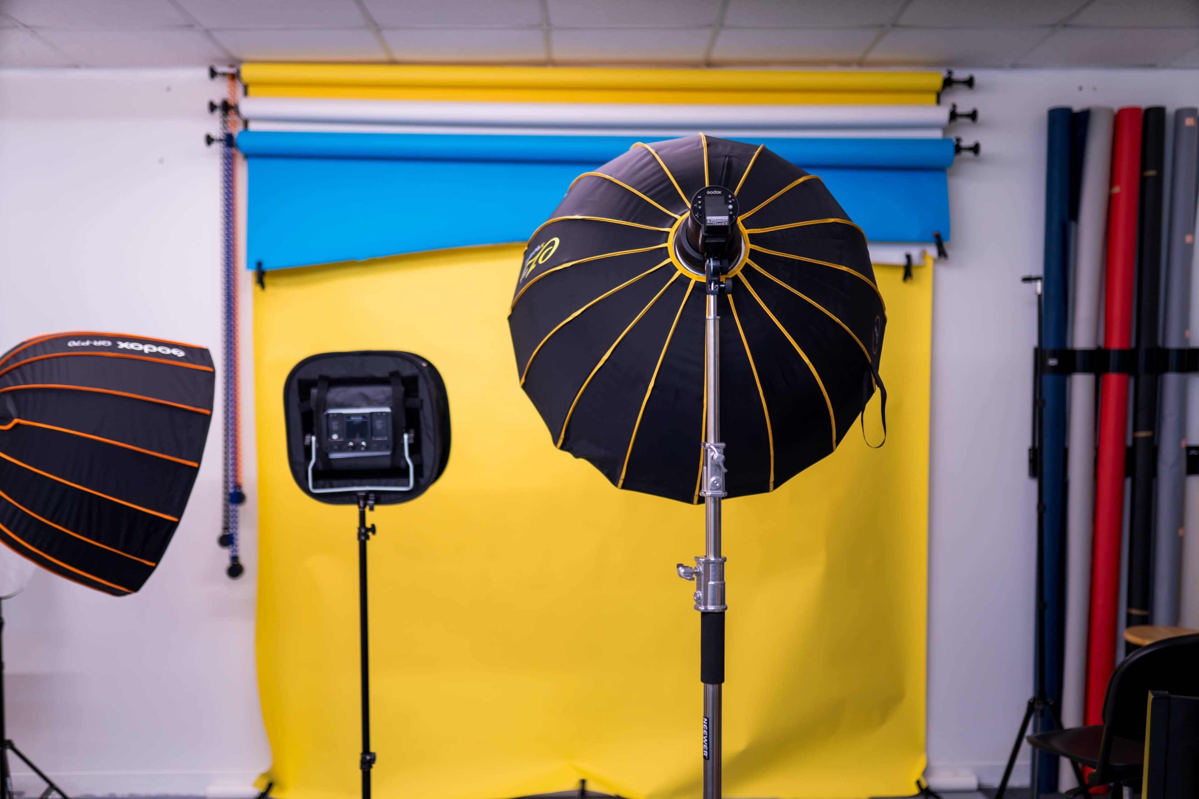 A photography studio setup featuring two lighting umbrellas and a backdrop of blue and yellow colors.