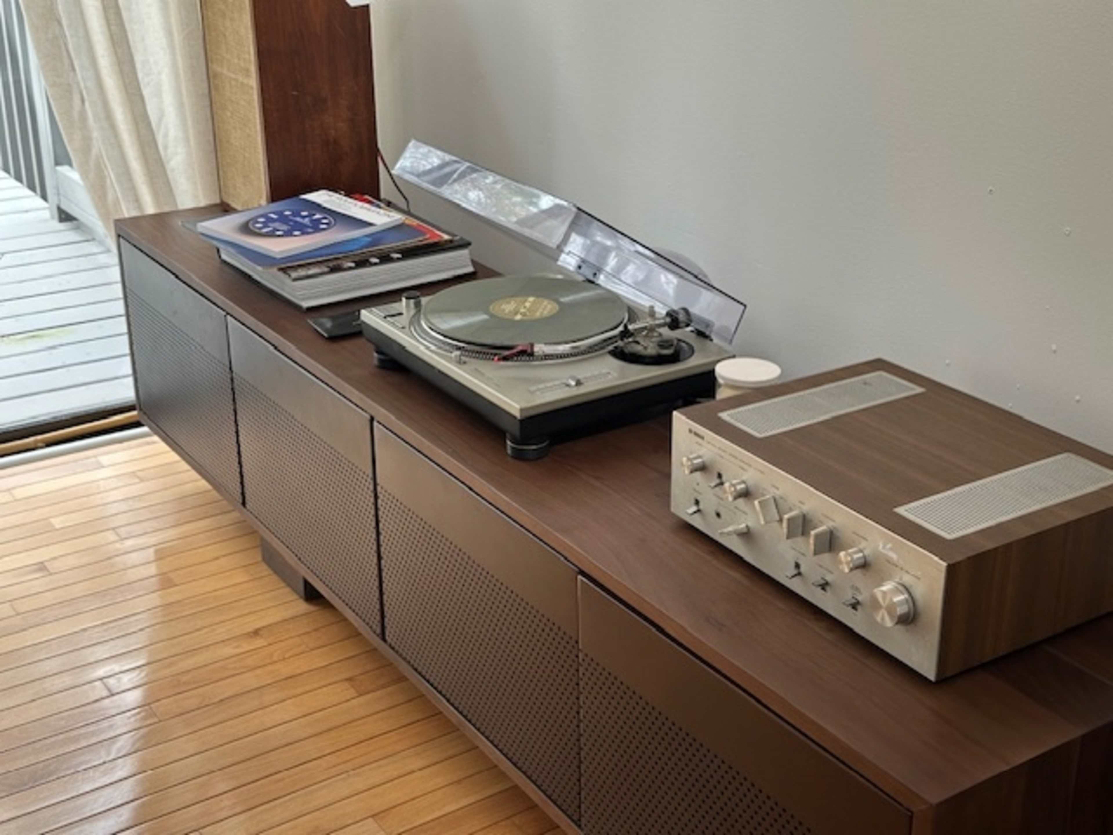 The image features a wooden console with a vinyl record player and an audio receiver, accompanied by several records on top.