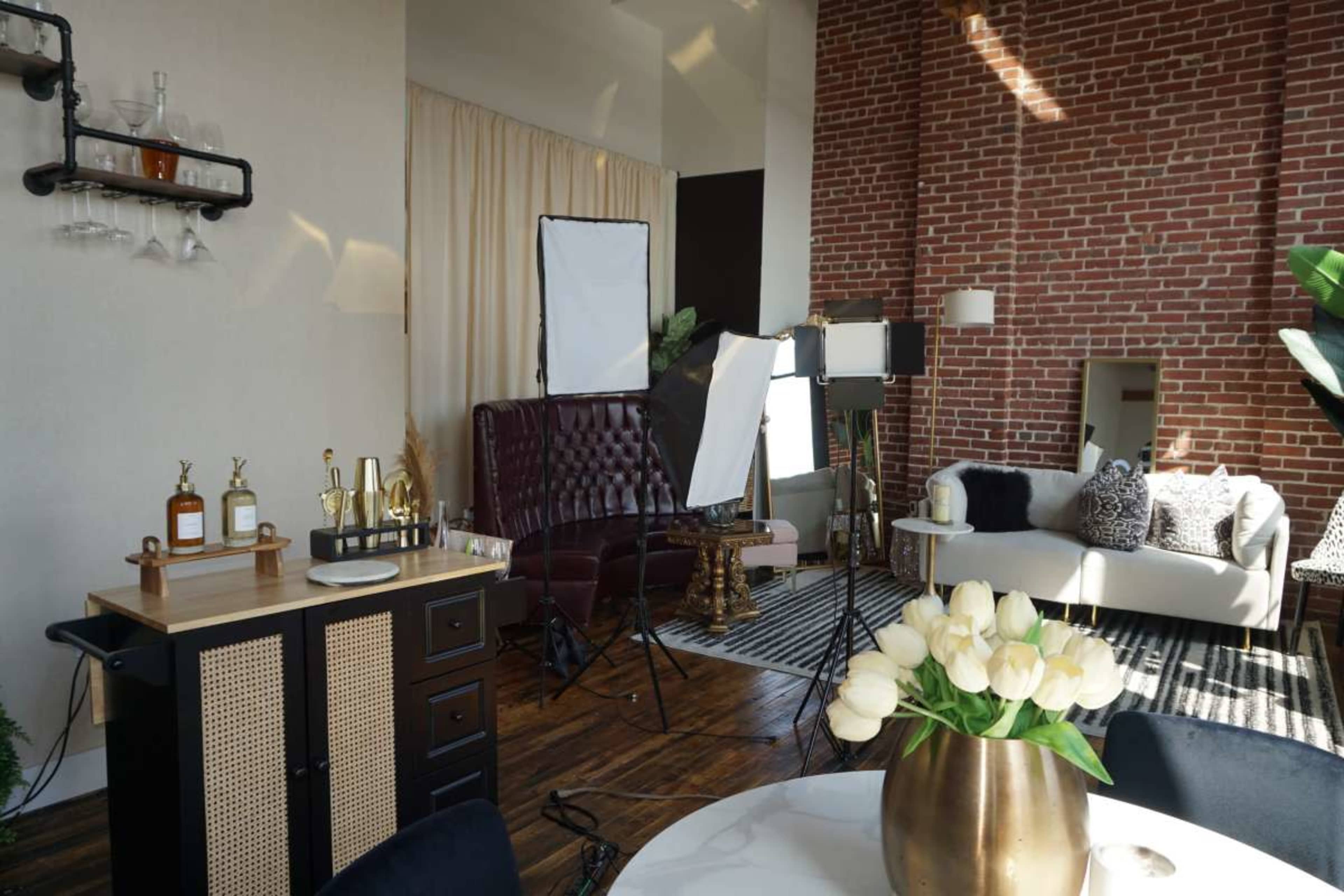 A styled interior space featuring a mix of modern and vintage furniture, photography equipment, and decorative elements like a large vase of white tulips on a round table.