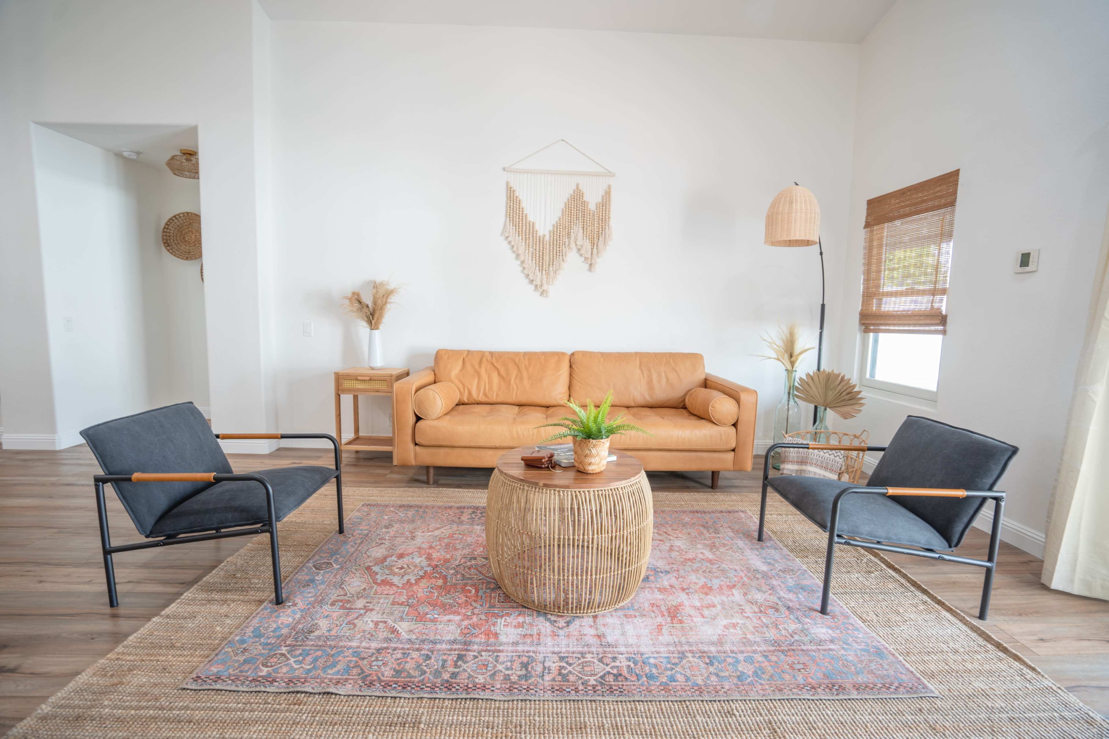 A stylish living room features a leather couch, two black chairs, a round woven coffee table, and a decorative rug on a wooden floor.