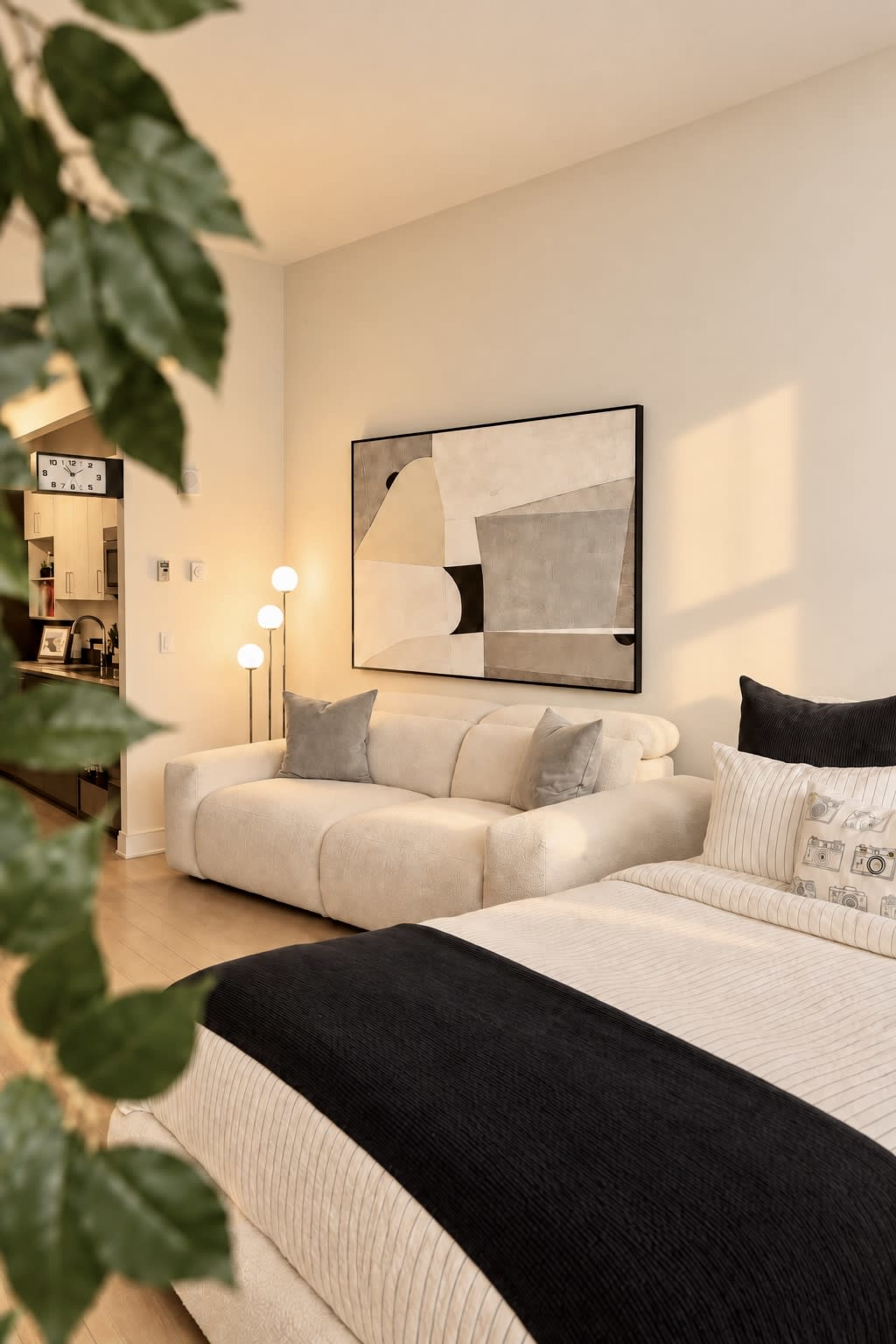 The image shows a modern bedroom featuring a large bed with dark and light bedding, a stylish couch, and a piece of abstract art on the wall.