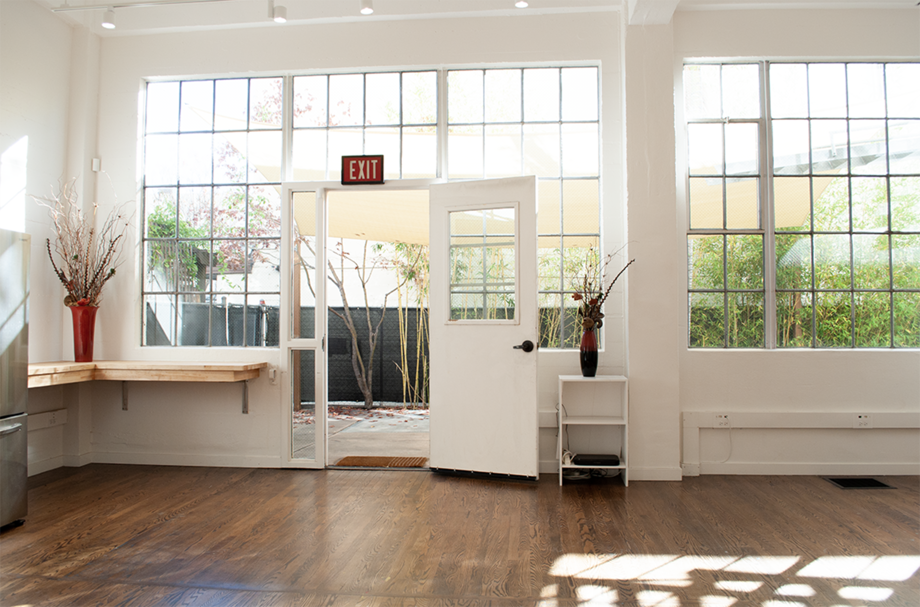 A bright, airy room with large windows, a white door leading outside, and wooden flooring.