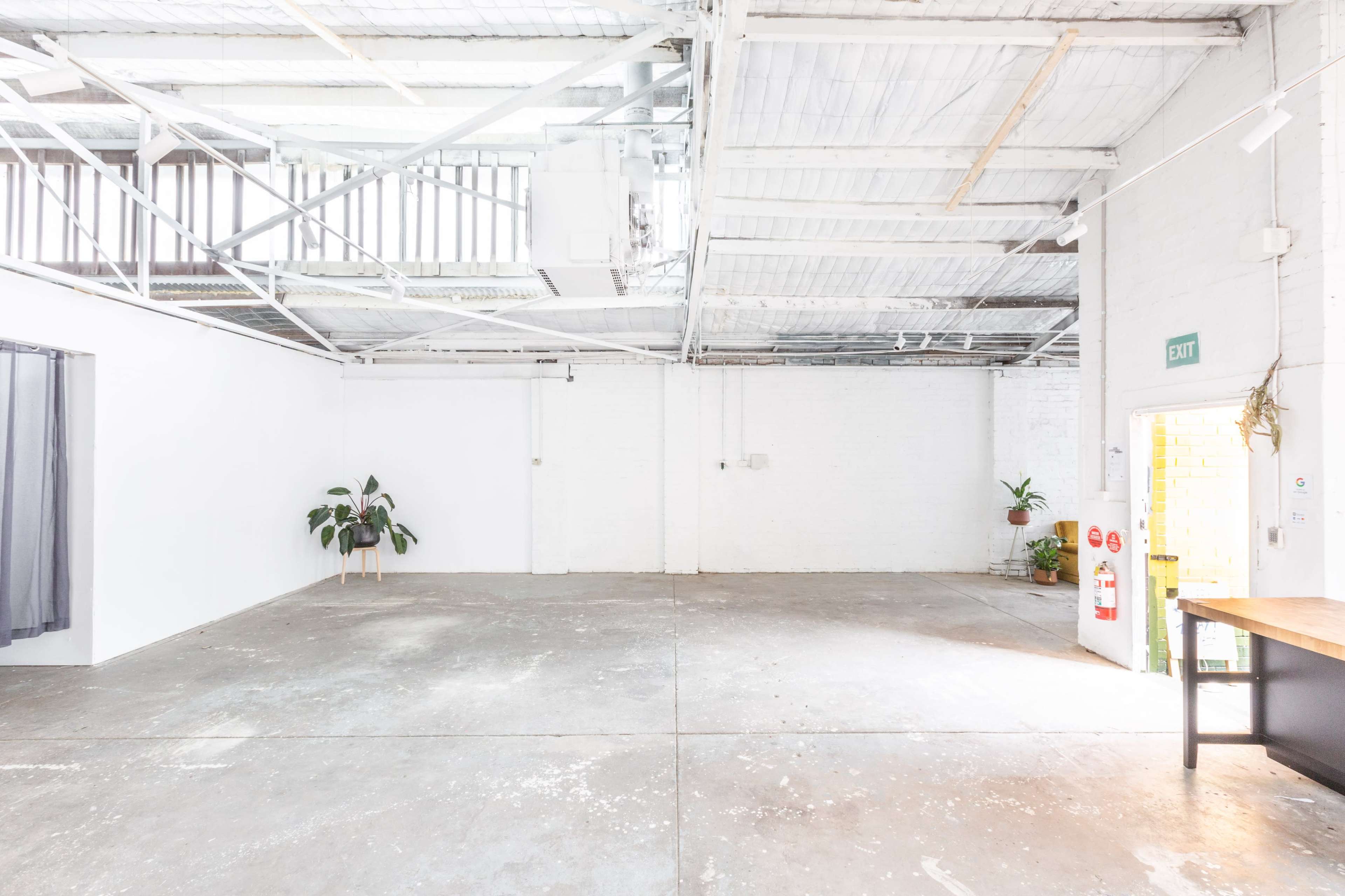 A spacious, empty industrial room with white walls, concrete flooring, and a few indoor plants in the corner.