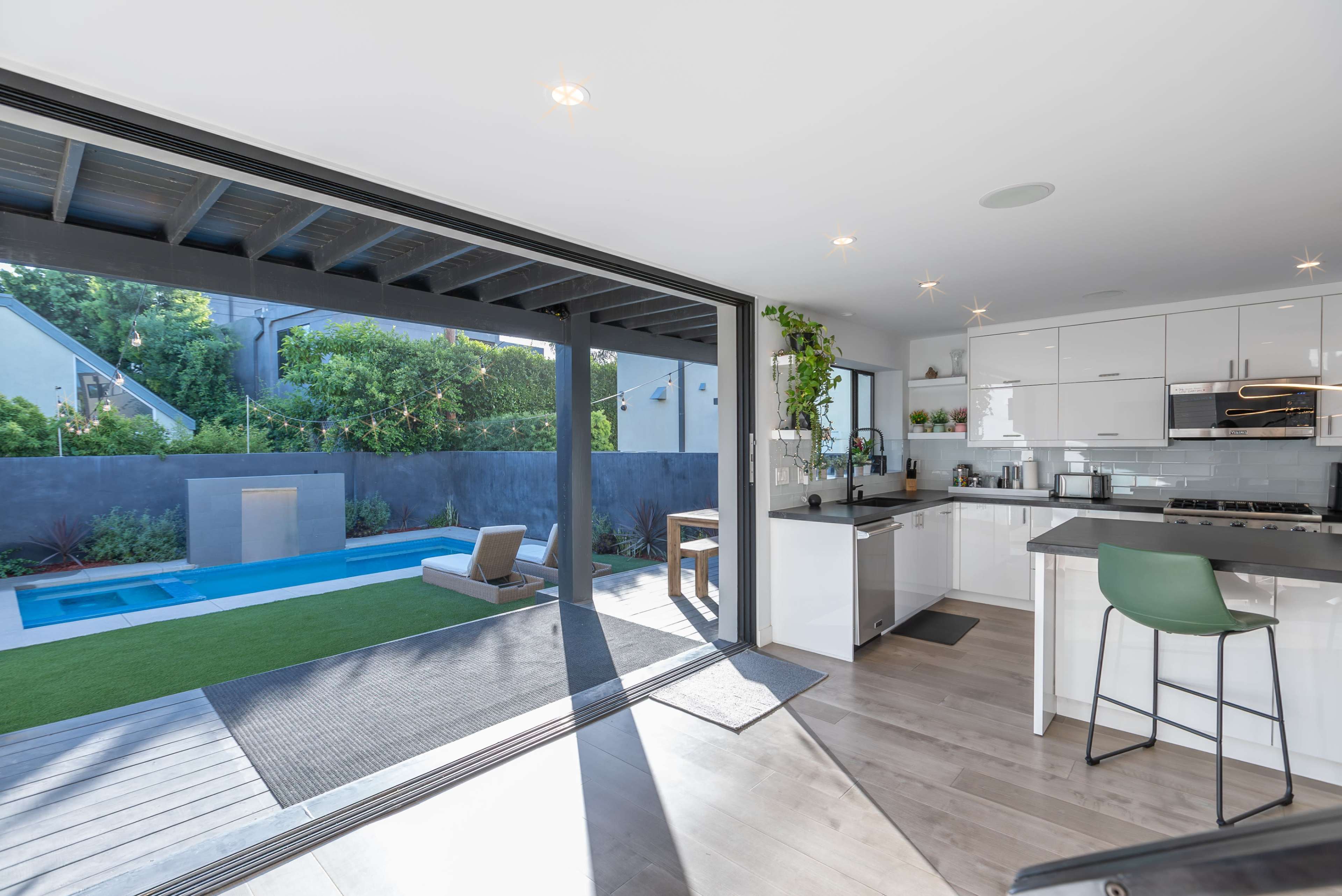 A modern kitchen features a sliding glass door opening to a landscaped outdoor area with a pool and lawn.