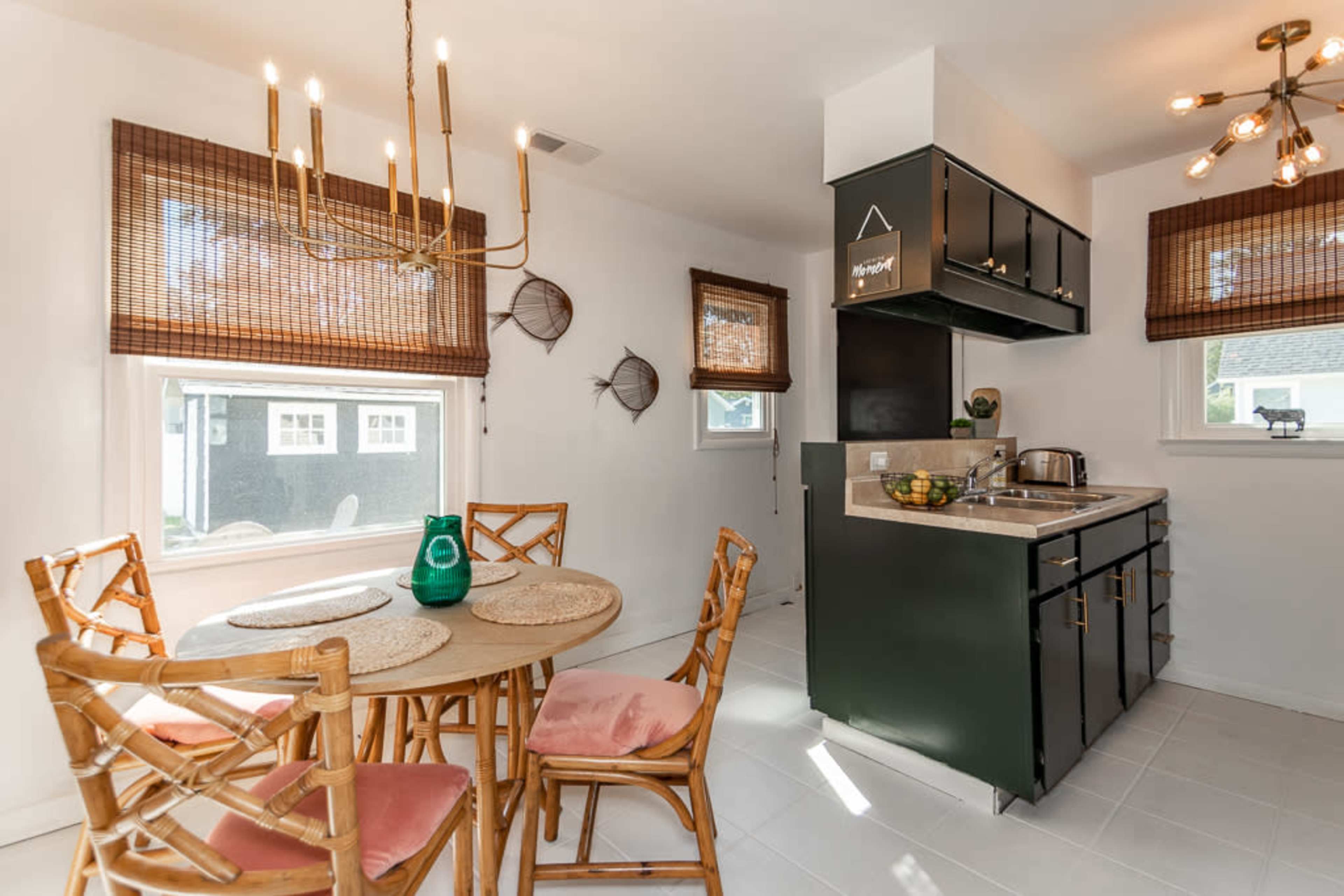 A small kitchen area featuring a round wooden table with four chairs, a light fixture hanging above, and a compact countertop with cabinets and kitchen appliances.