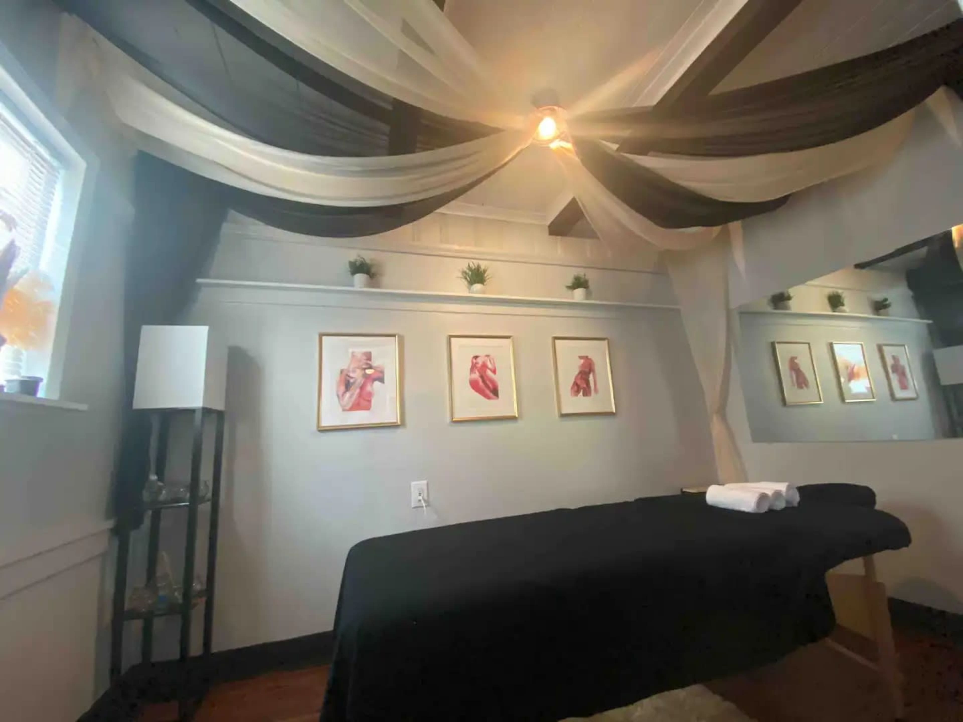 A massage room with a treatment table, decorative framed artworks on the wall, and soft lighting.