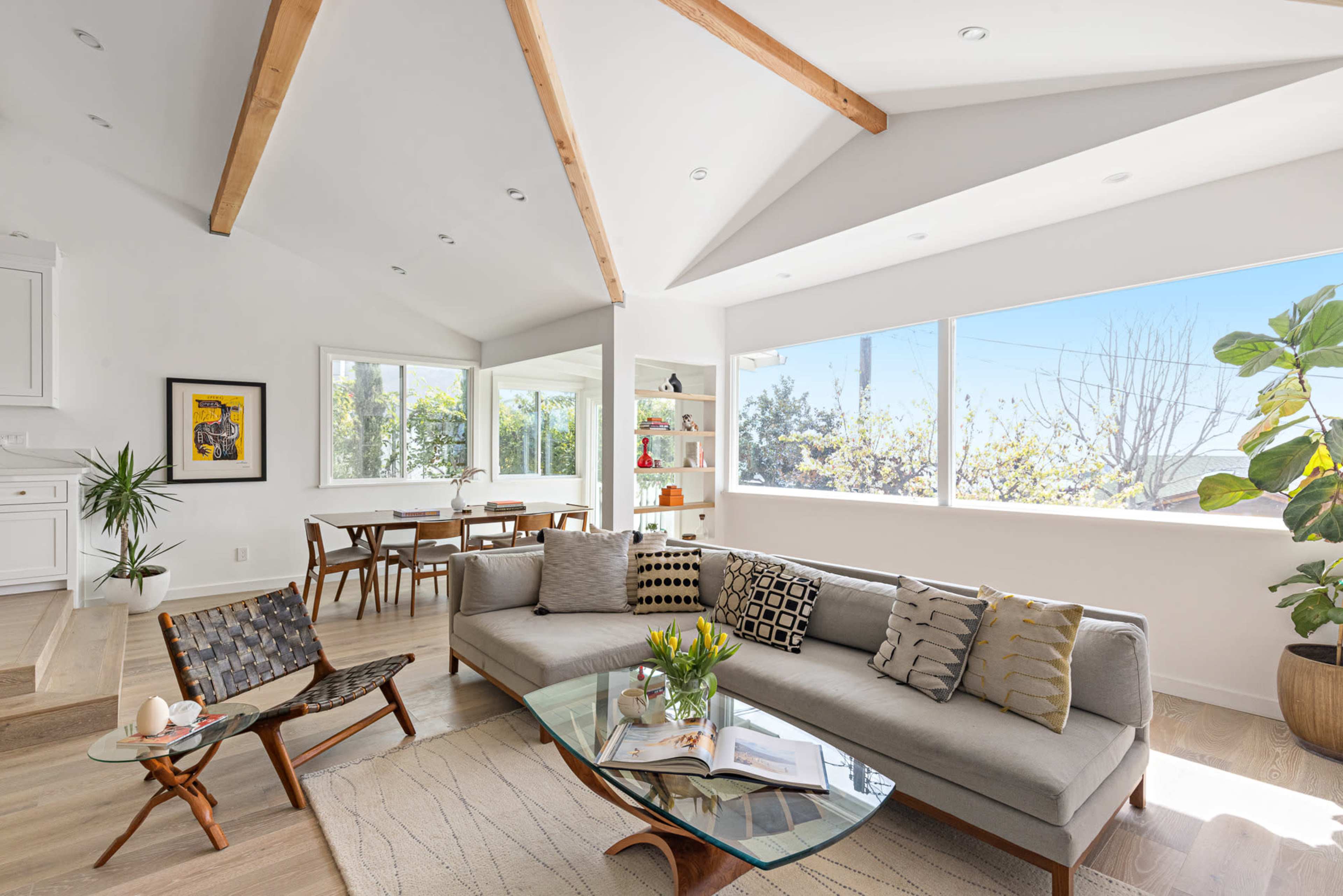 A modern living room with a sectional sofa, a glass coffee table, and large windows allowing natural light to fill the space.