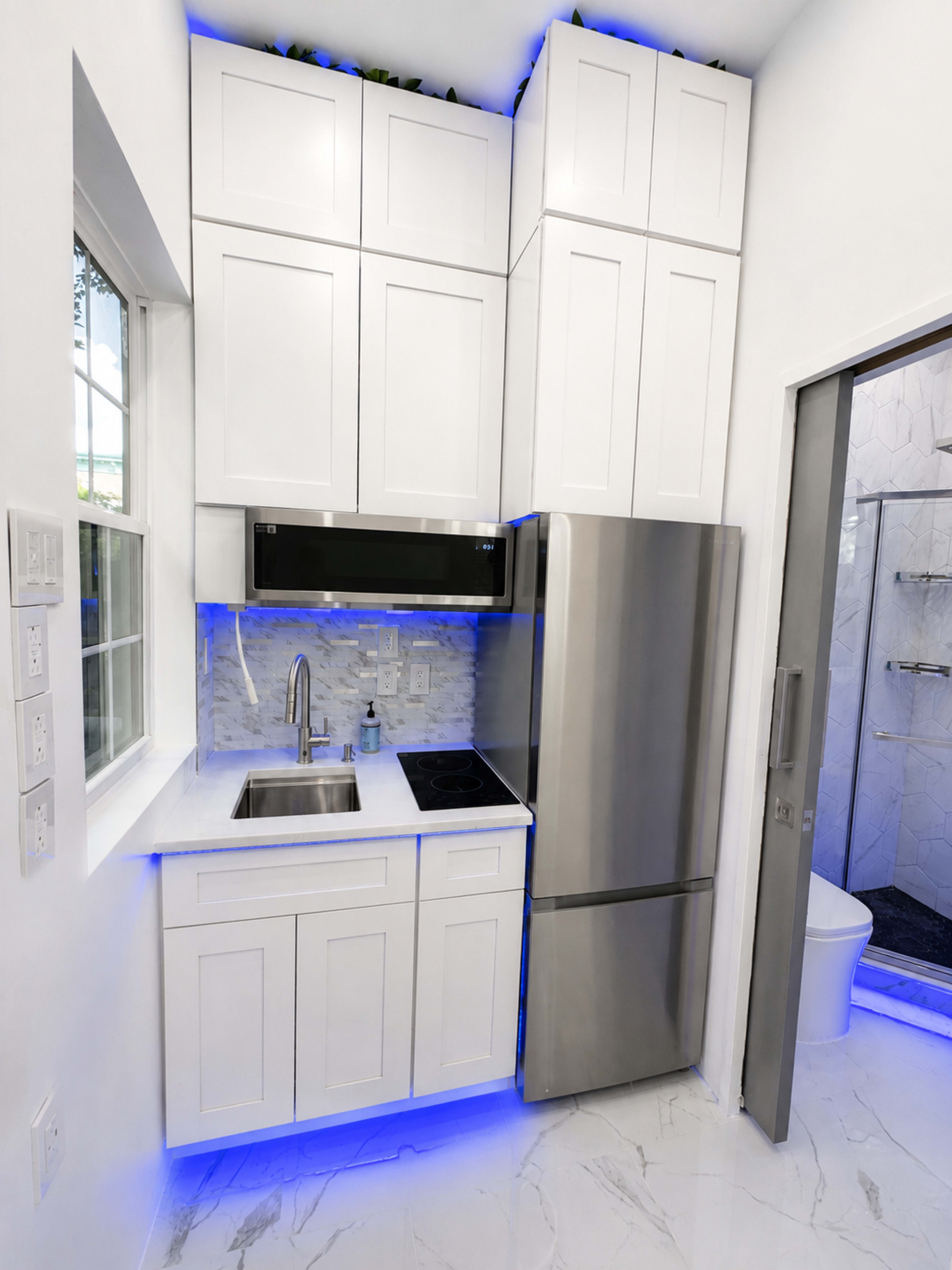 The image features a modern kitchen with white cabinets, stainless steel appliances, and blue LED lighting along the countertops and cabinetry.