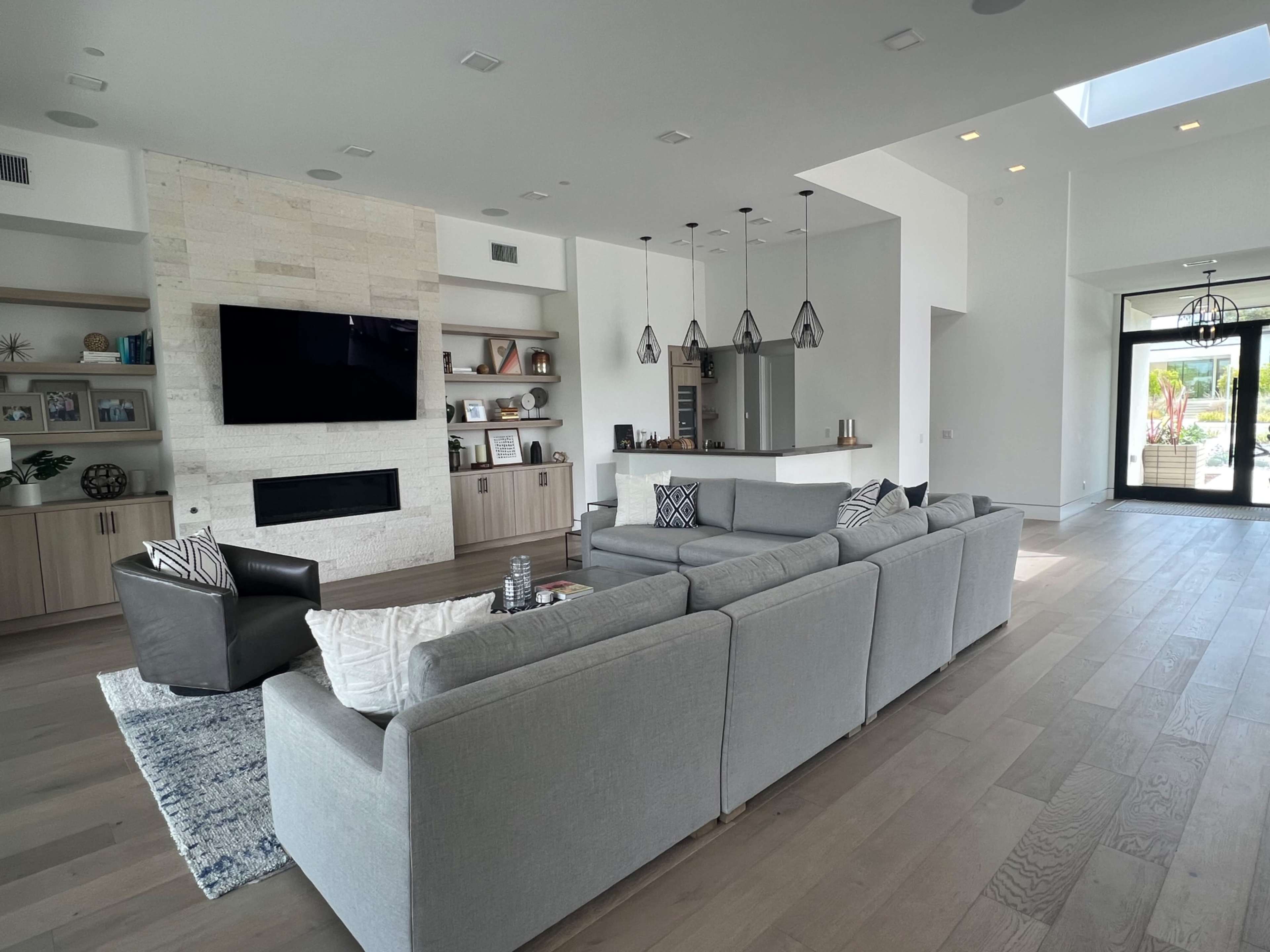 A modern living room featuring a large sectional sofa, a wall-mounted television, and a fireplace, with an adjacent open kitchen area visible in the background.