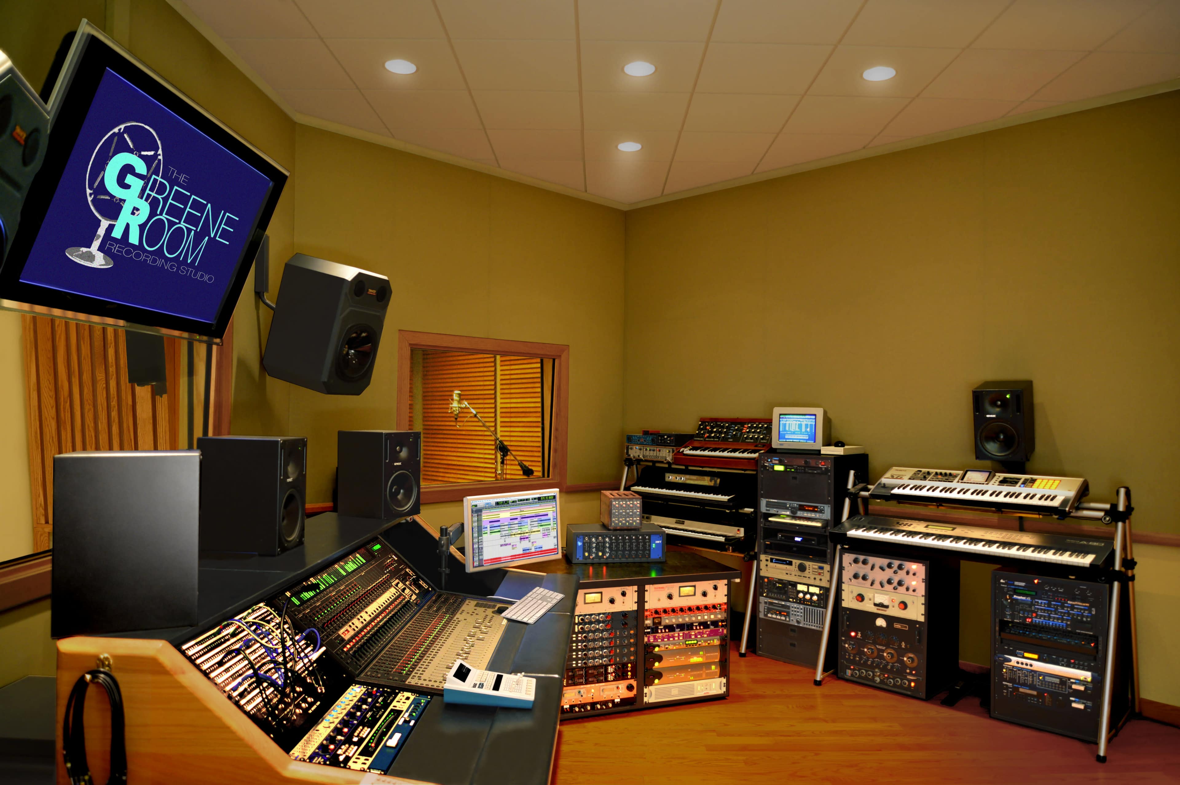 A well-equipped recording studio featuring a large mixing console, various synthesizers, and audio equipment arranged in a soundproof room.