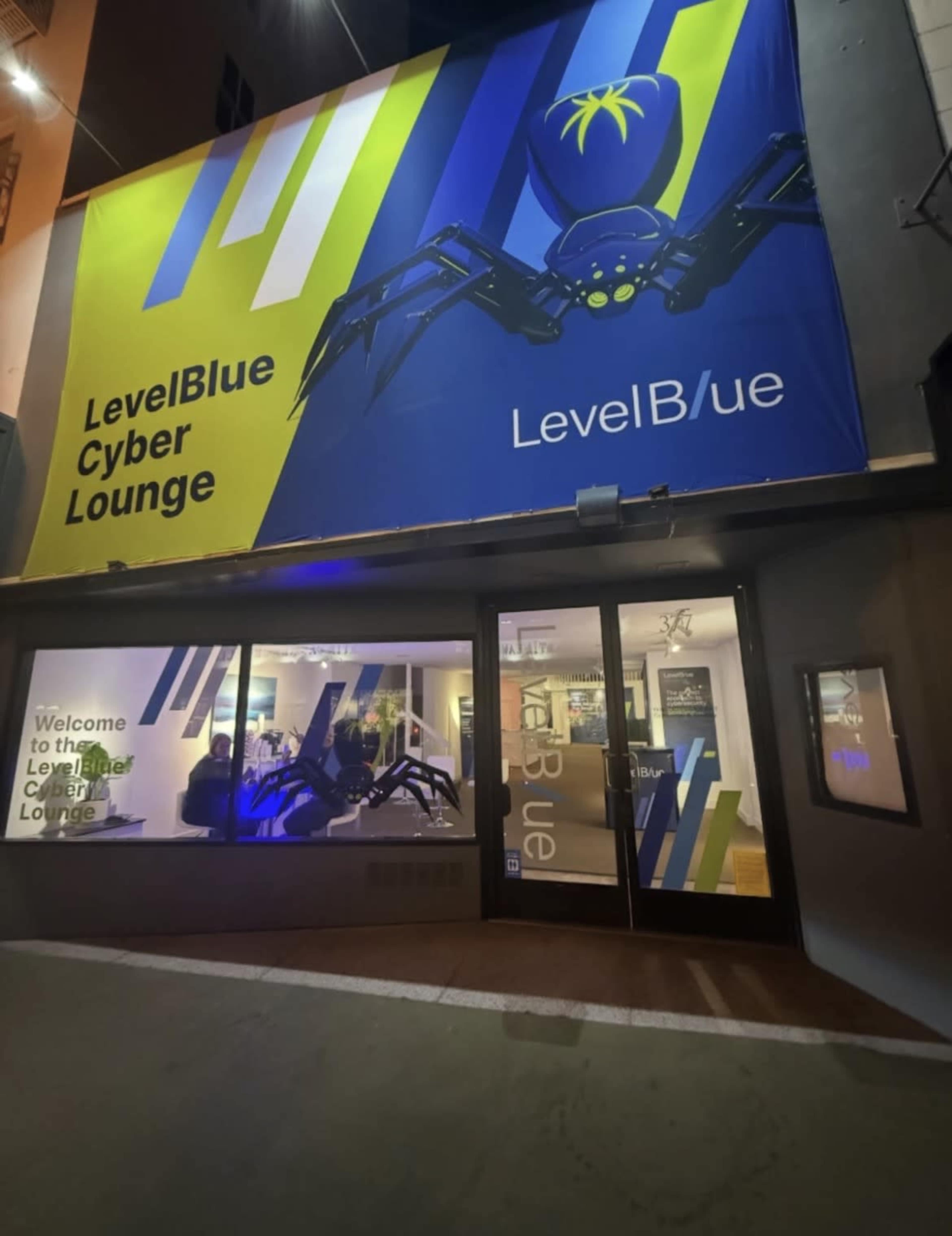 The image features a large, vibrant banner displaying a spider logo and the text "LevelBlue Cyber Lounge" above a glass entrance with the same branding.