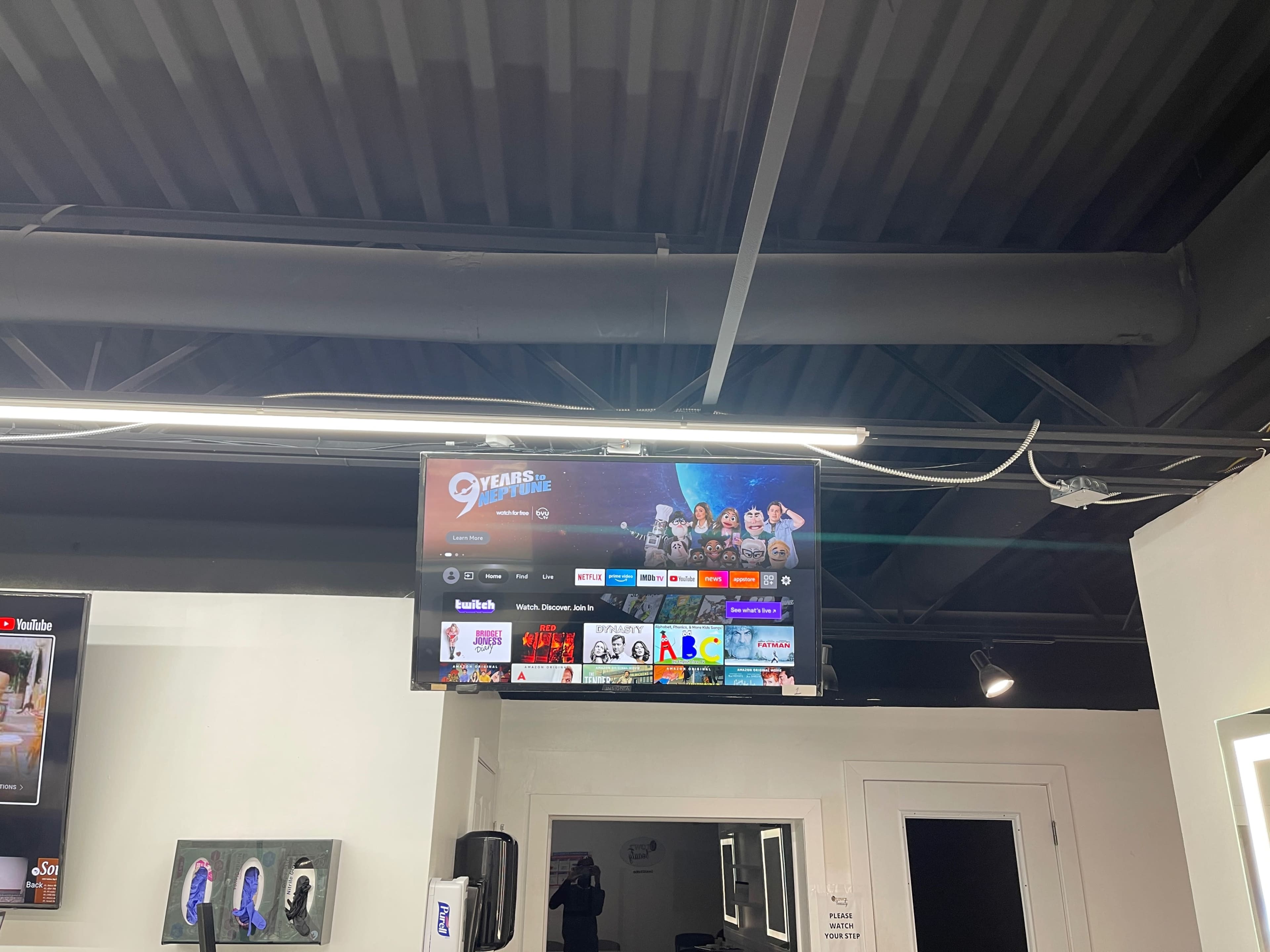 A flat-screen TV mounted on the wall displays a streaming service interface with various show and movie options.