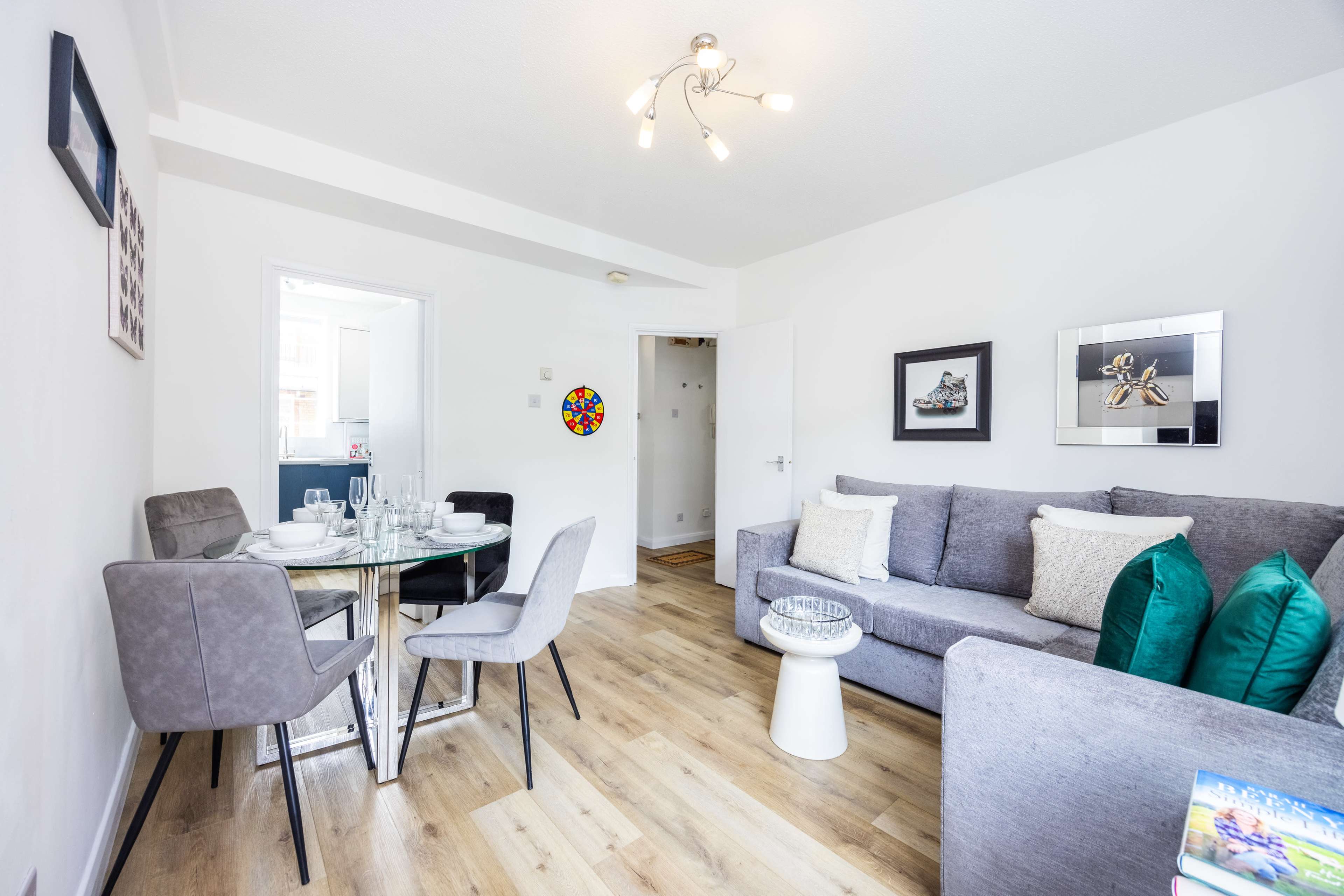 A modern living space features a gray sofa, a glass dining table with chairs, and light wood floors.