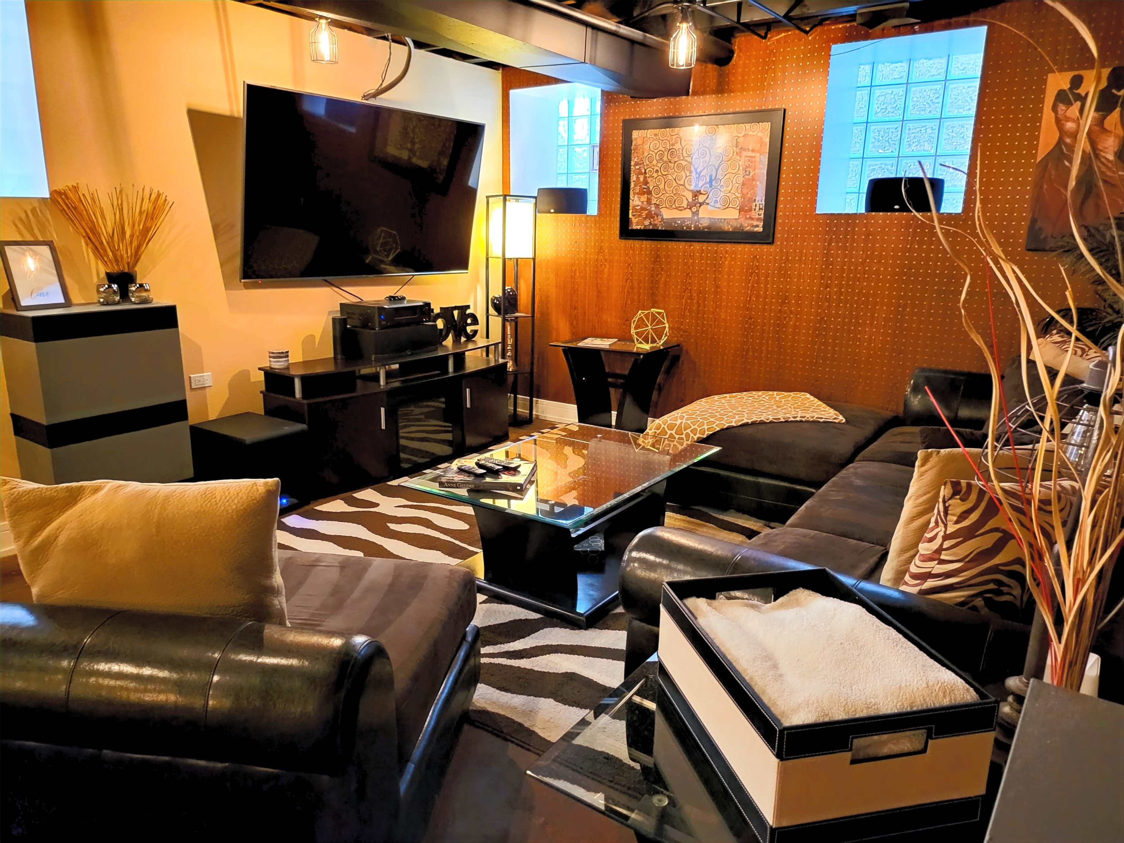 A cozy living room with a sectional sofa, a large television on the wall, and a glass coffee table surrounded by decorative elements.