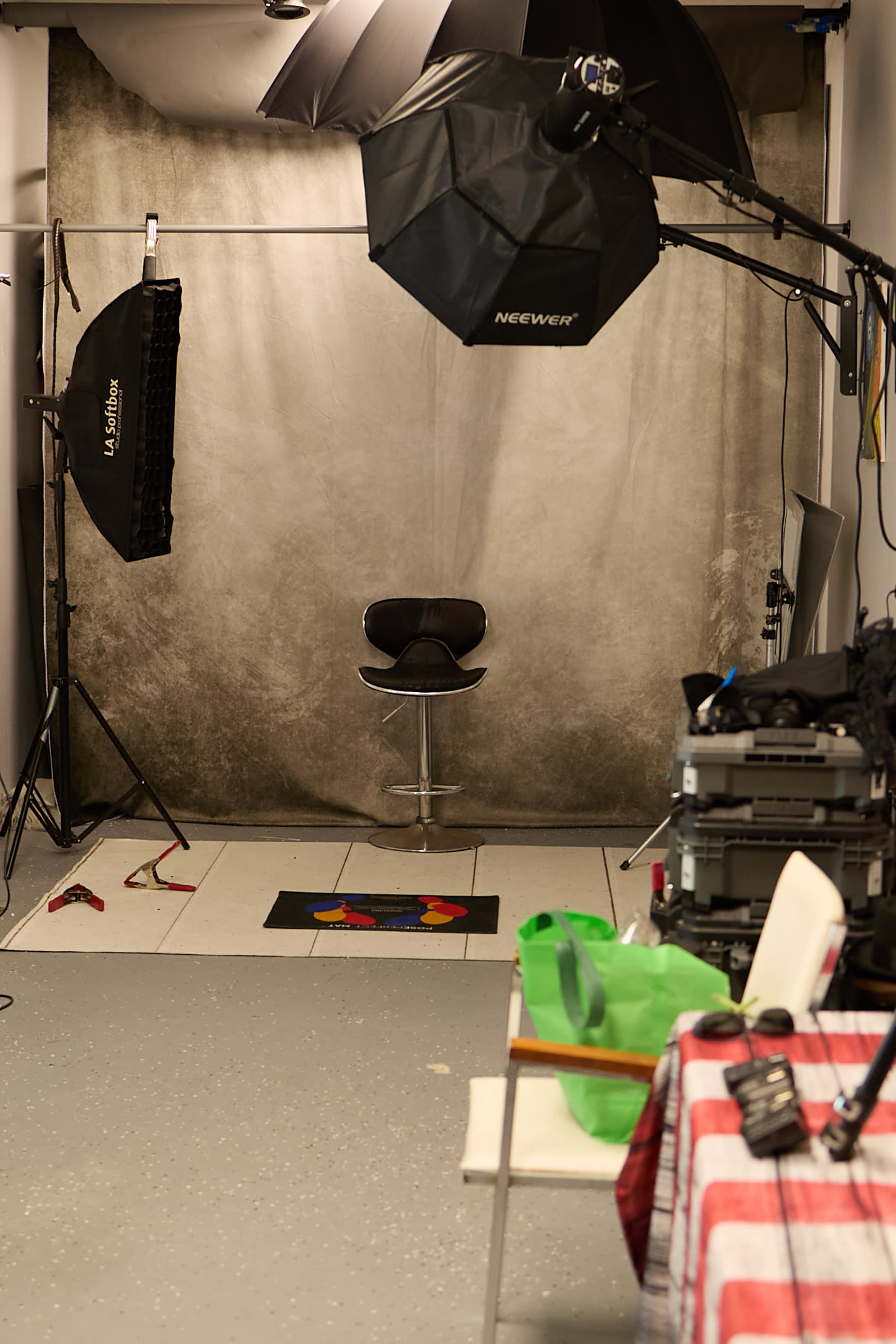 The image shows a photography studio equipped with lighting equipment, a backdrop, a stool, and various props scattered around.