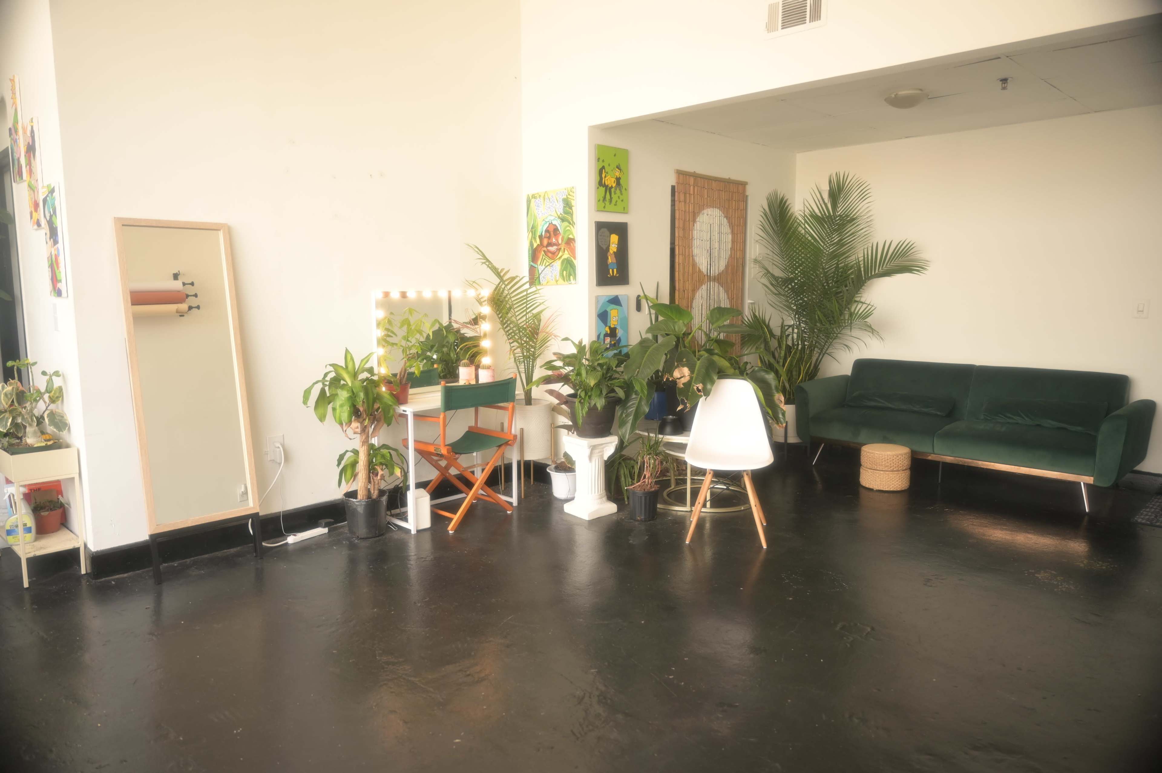 A bright interior space featuring a green couch, various indoor plants, a mirror, and a small vanity table with a chair.