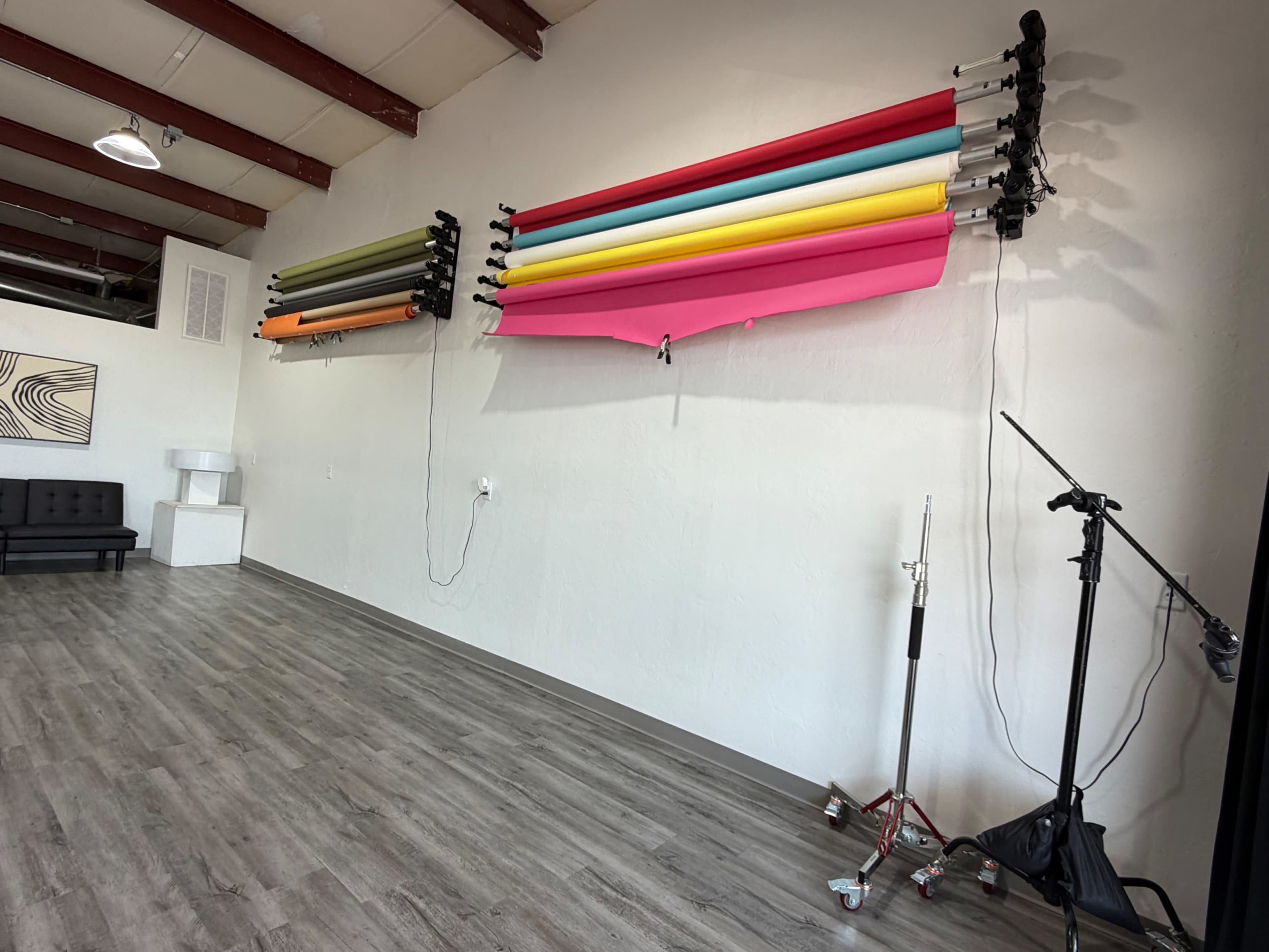 The image features a spacious studio with colorful backdrops mounted on the wall and a black sofa positioned on the left.