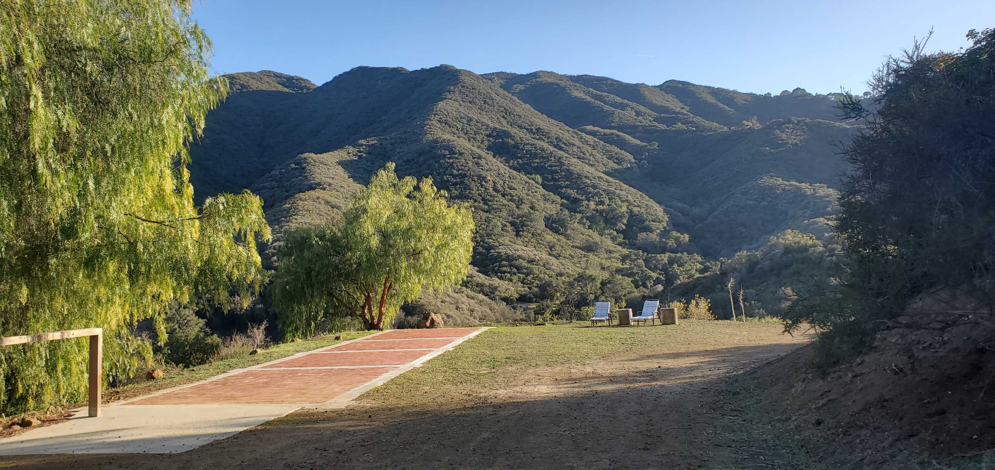 The image features a serene outdoor scene with a paved area and two chairs overlooking a mountainous landscape.