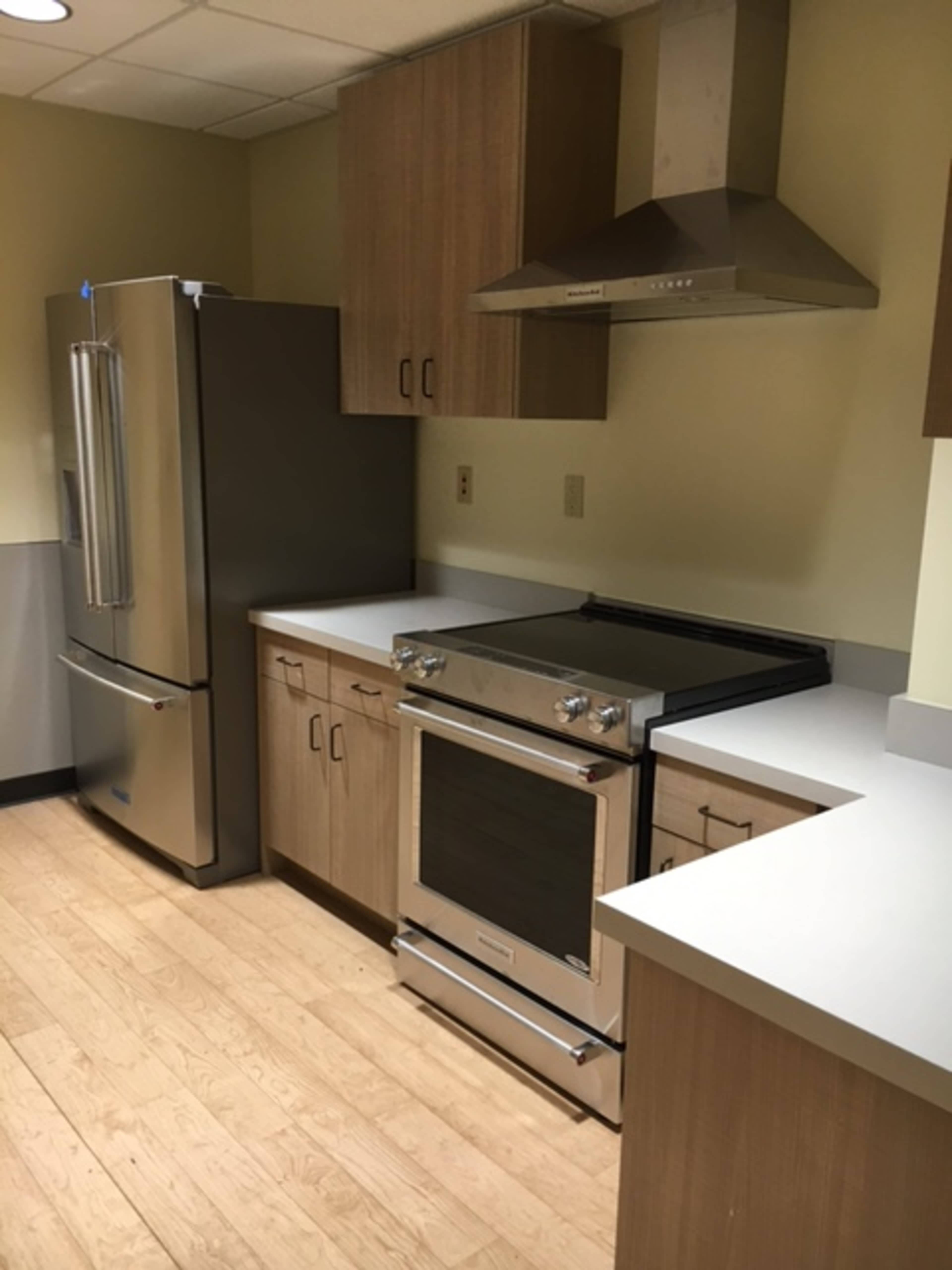 A modern kitchen with light wood cabinetry, a stainless steel refrigerator, an oven range, and a hood above it.