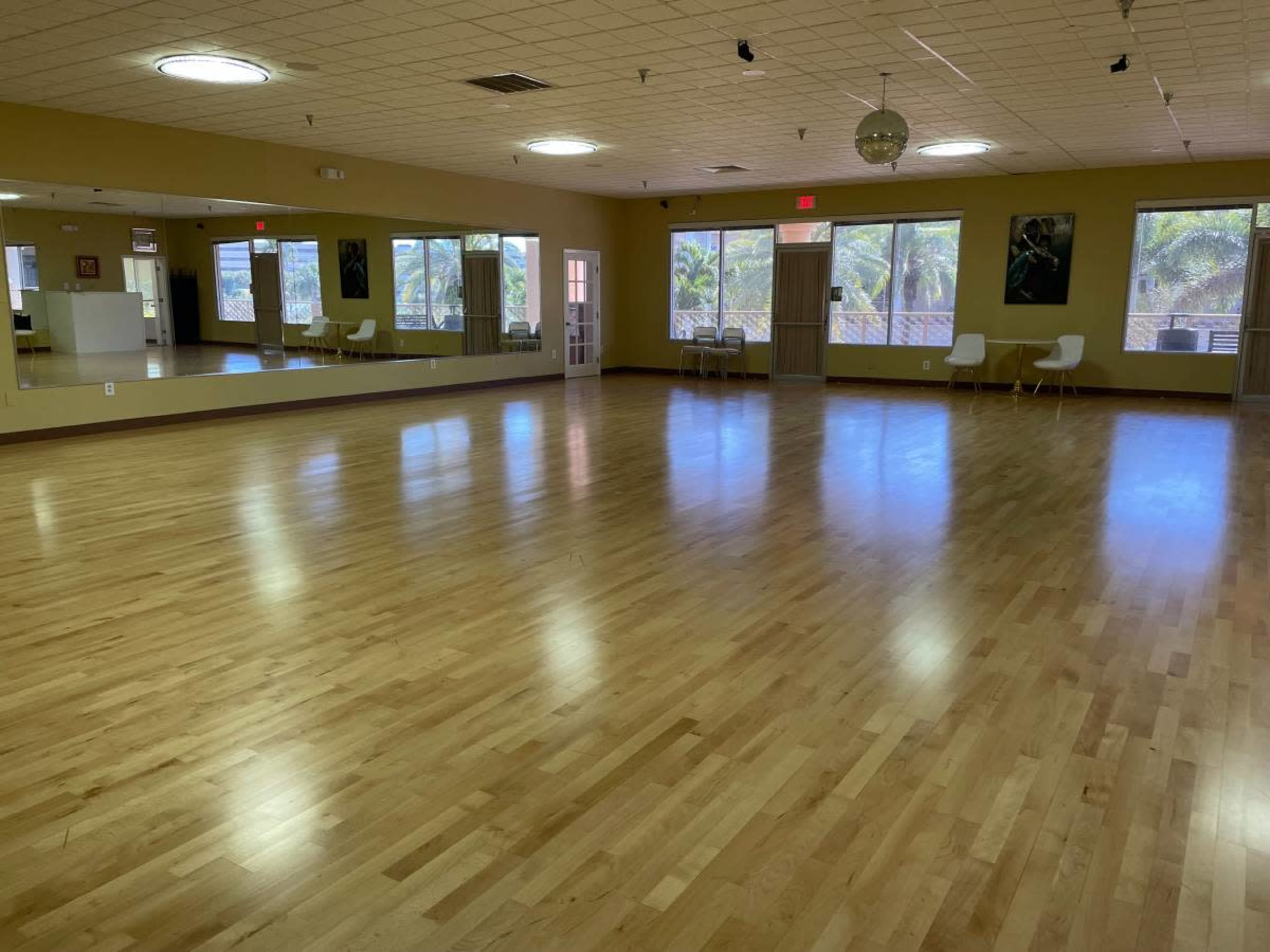 A spacious, empty dance studio with wooden flooring and large windows letting in natural light.