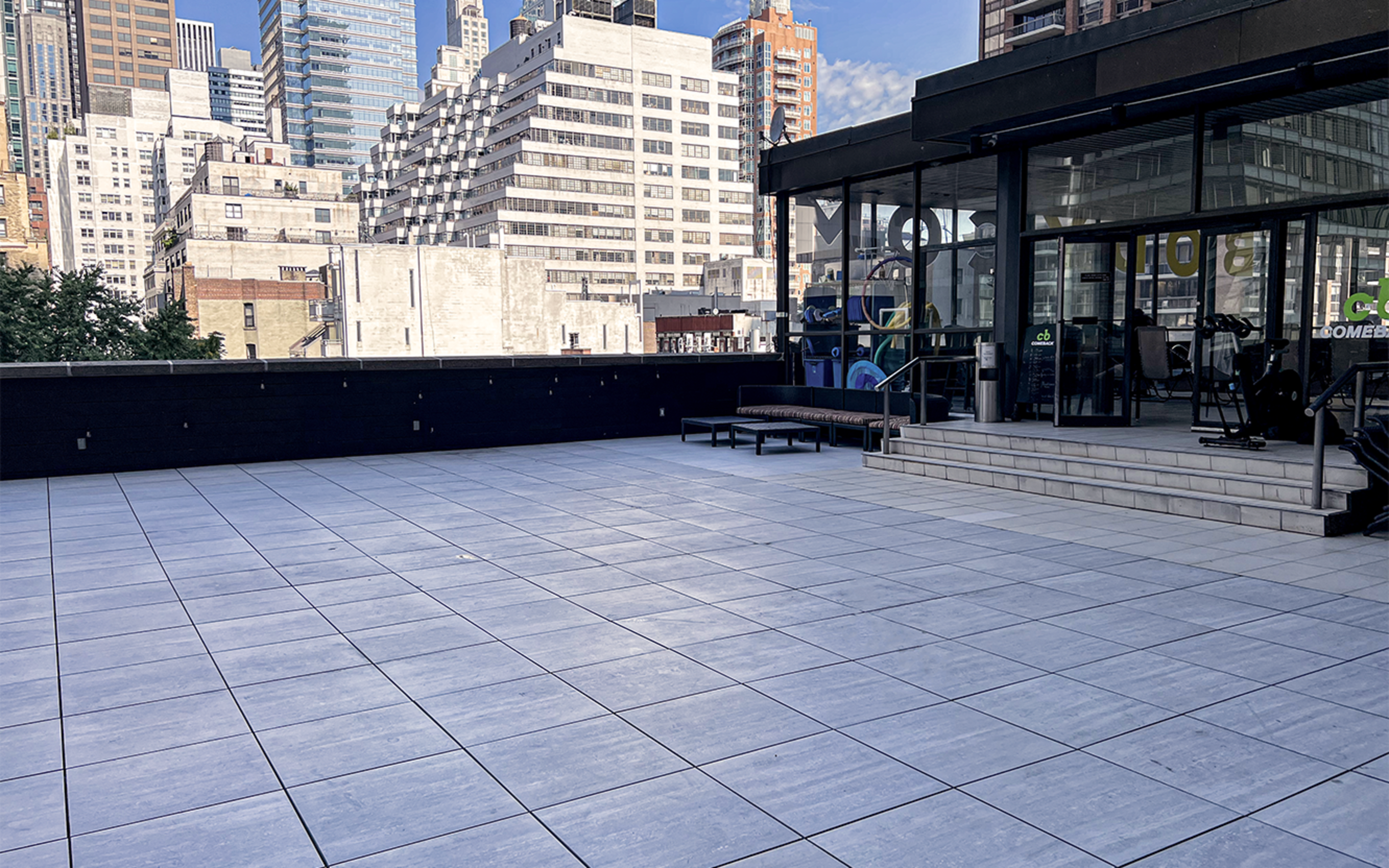 A spacious terrace with large, tiled flooring and a glass-walled building in the background, surrounded by urban high-rises.