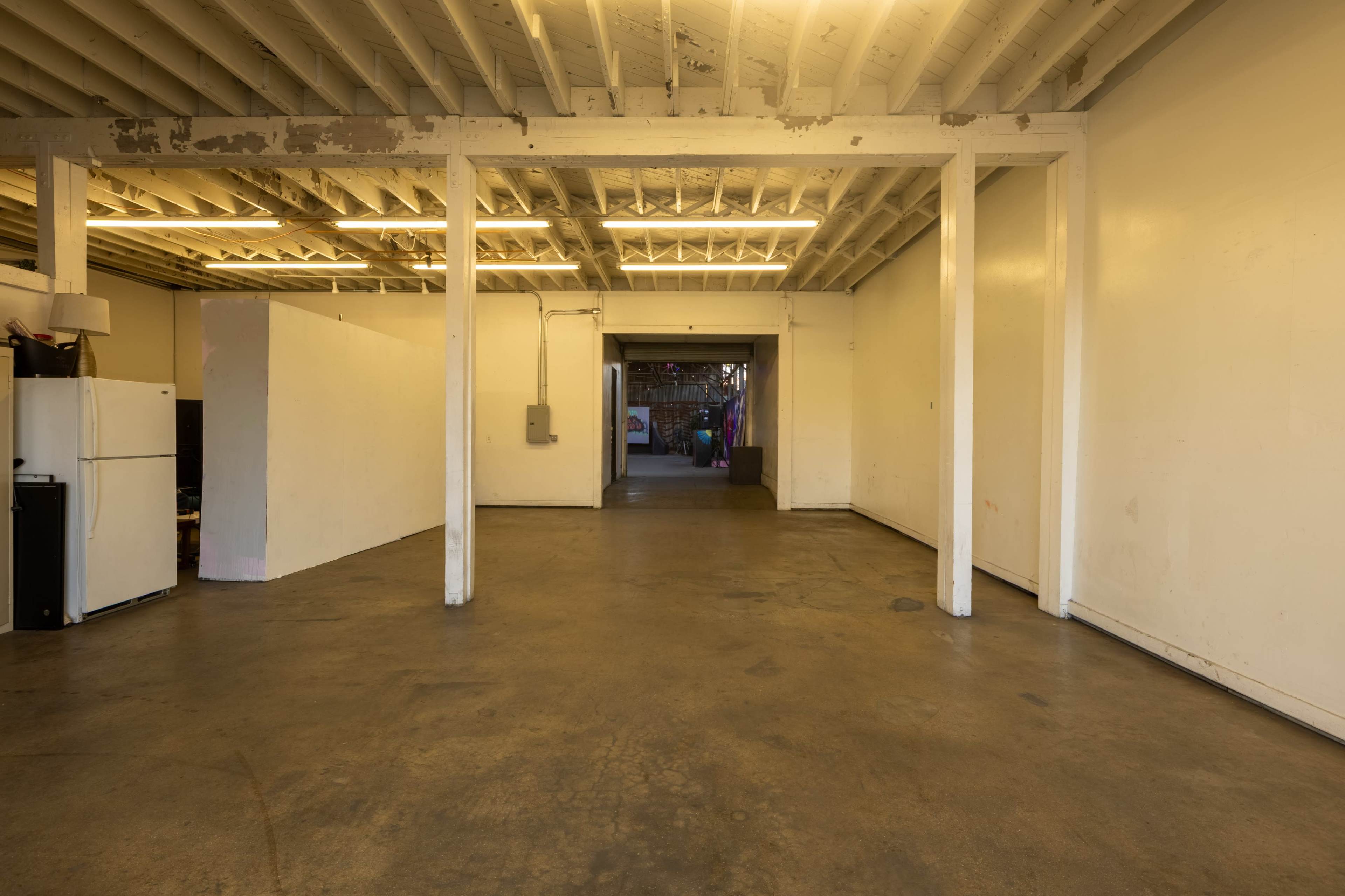 The image shows an empty, spacious industrial room with concrete flooring and exposed beams in the ceiling.