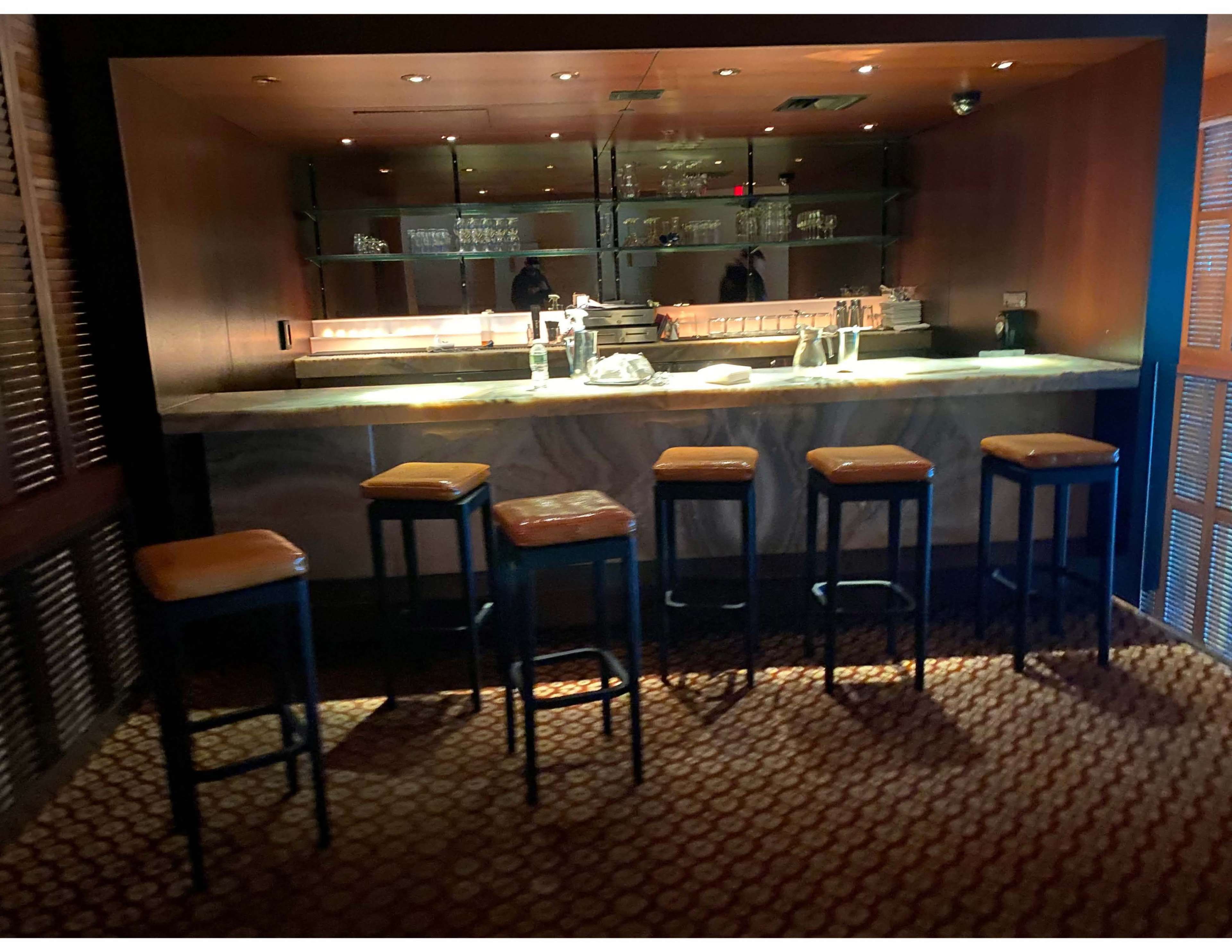 A dimly lit bar area features a long countertop with several empty stools arranged in front.