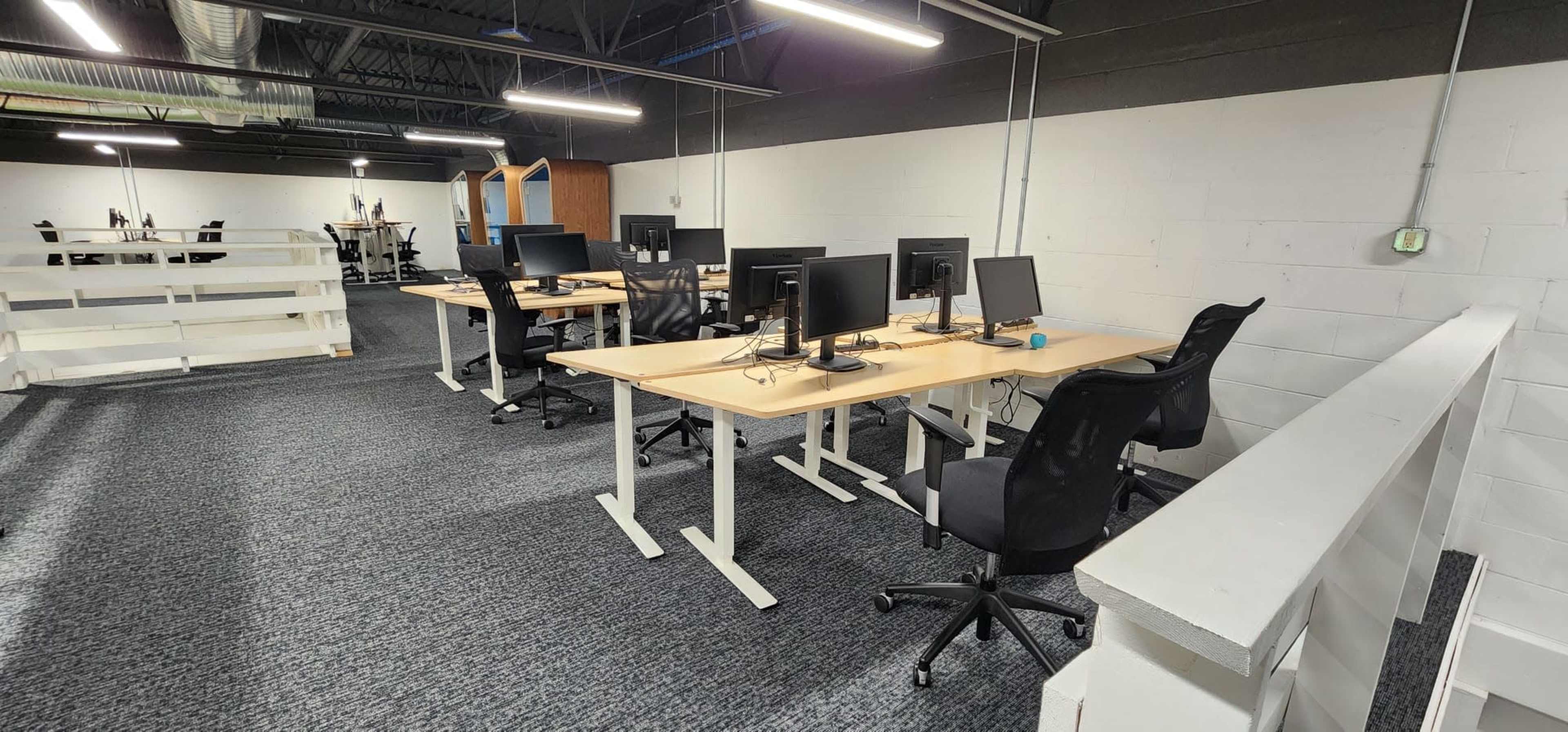 A row of empty desks with computers in an office space featuring gray carpeting and white walls.