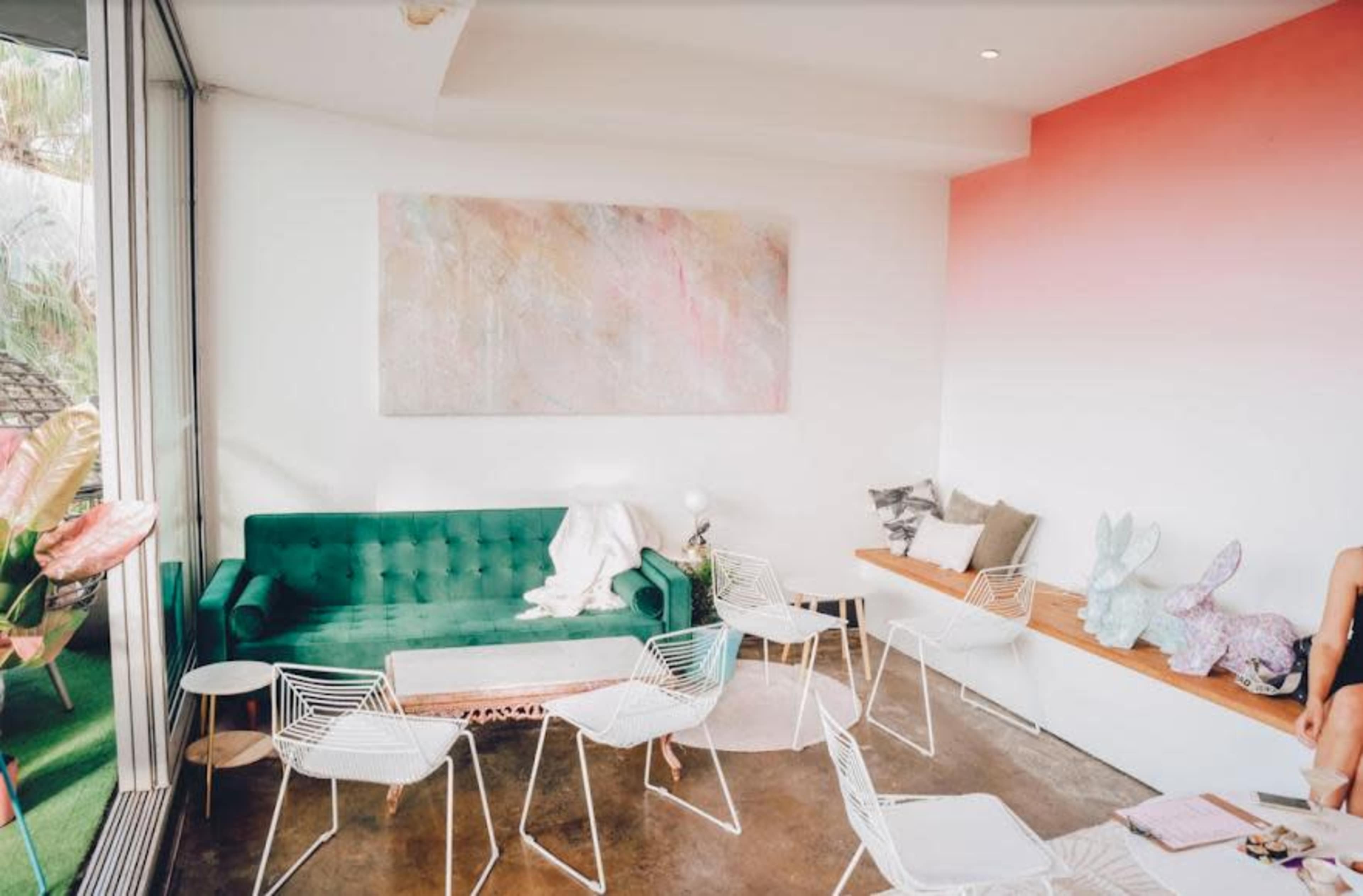 A modern lounge area with a green sofa, white chairs, and a large abstract painting on the wall, complemented by wooden seating and decorative items.