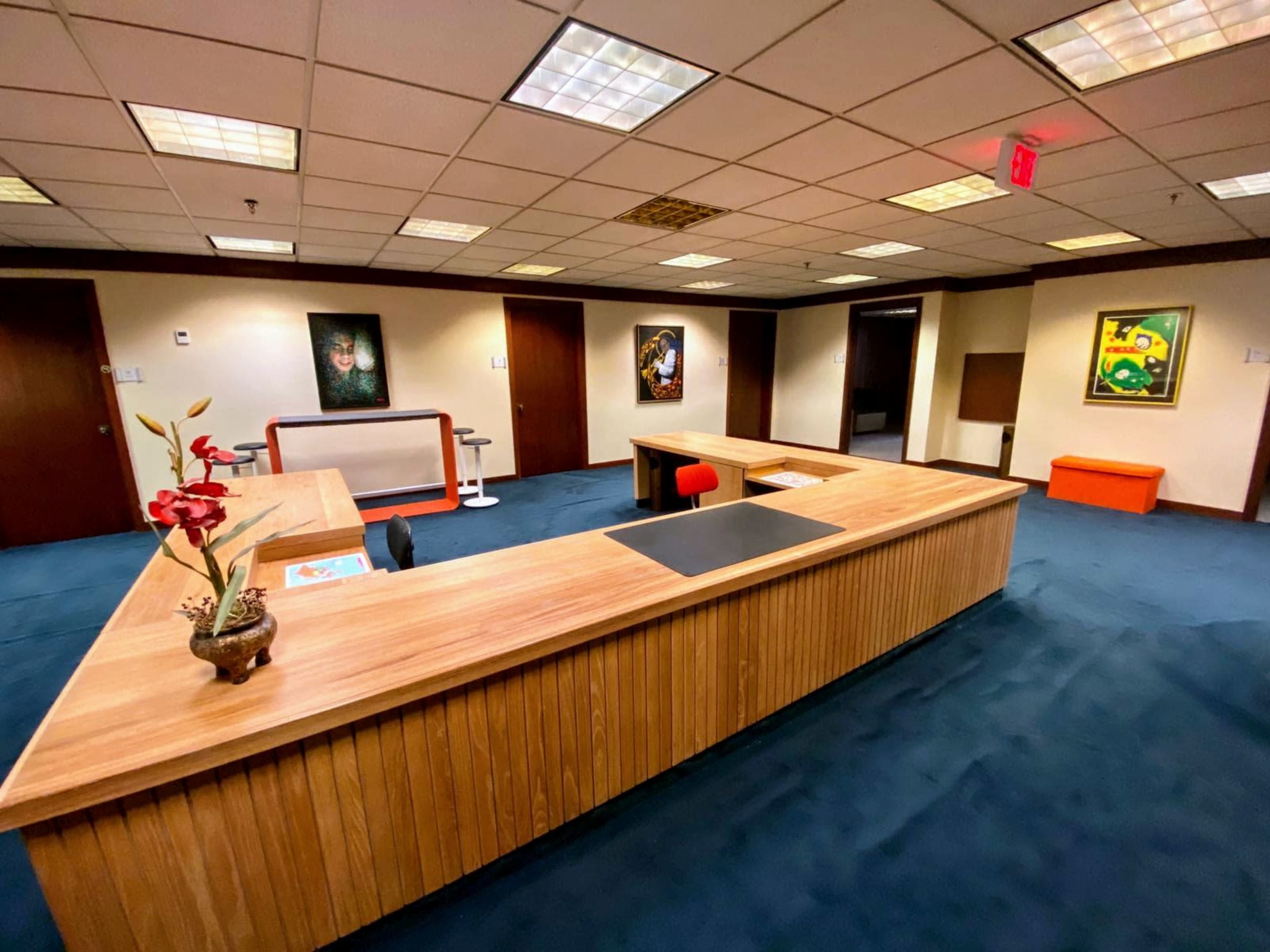An office space with a wooden reception desk, blue carpet, and several framed artworks on the walls.