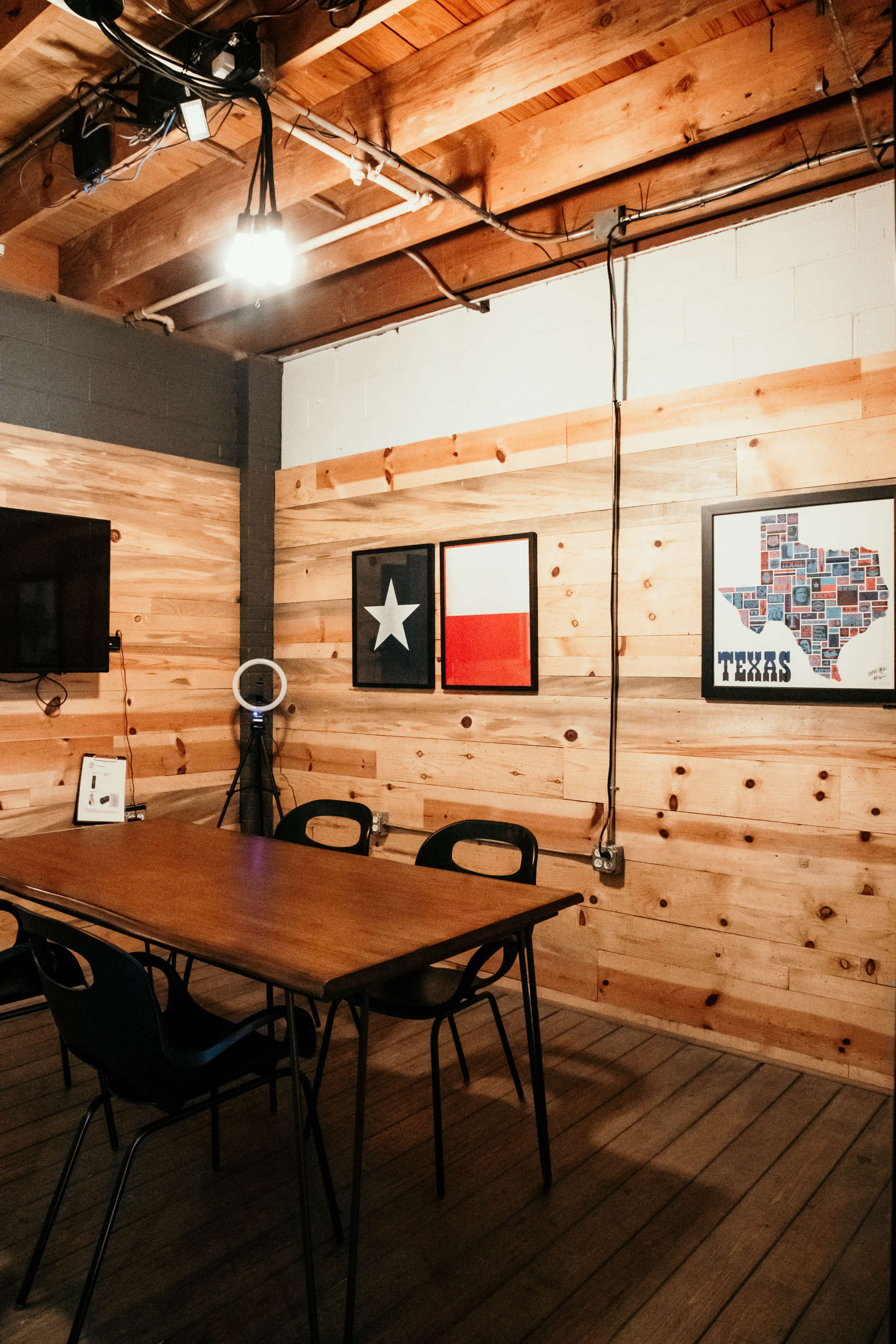 A wooden meeting room features a rectangular table surrounded by black chairs, with Texas-themed artwork on the walls.