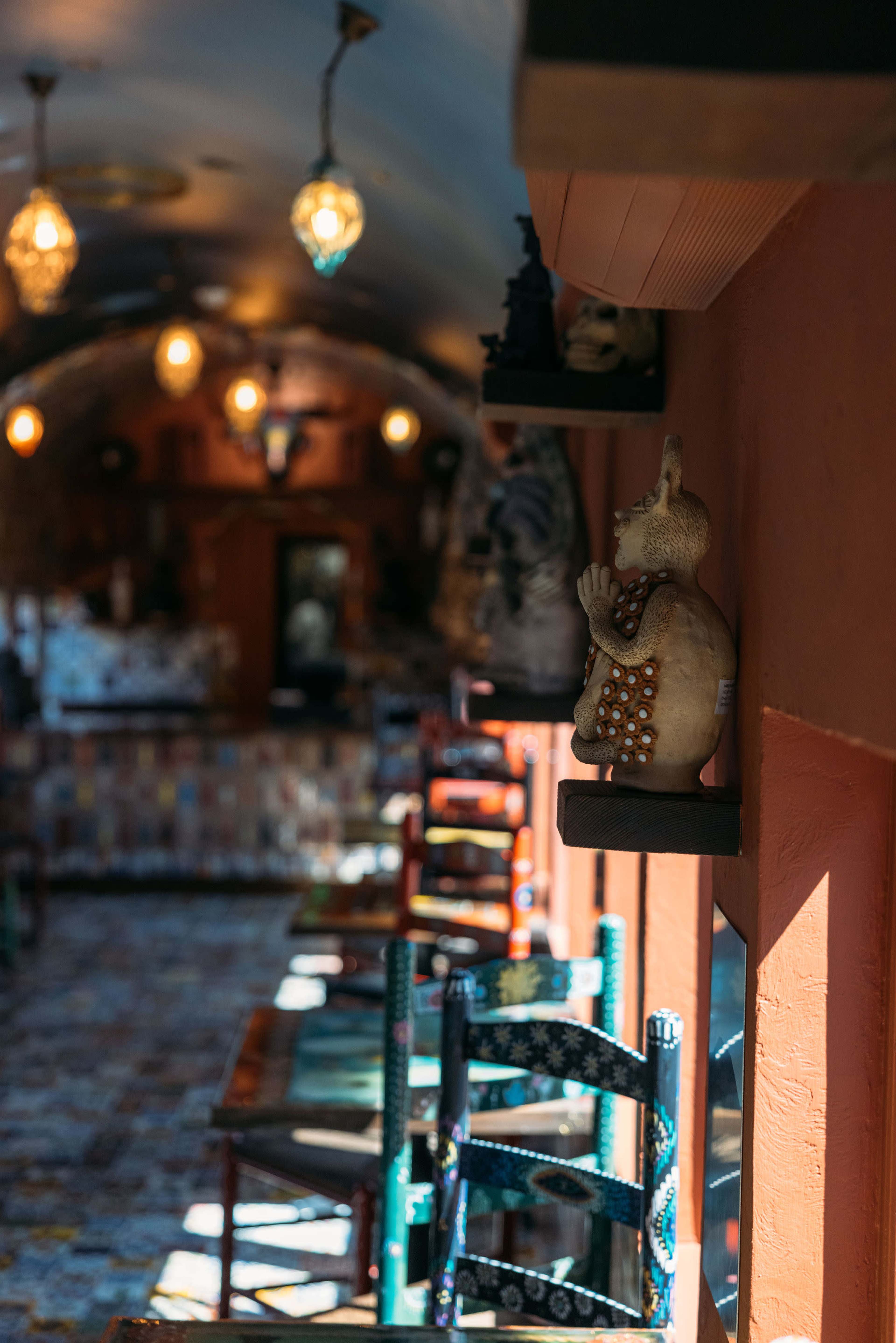 The image shows an interior of a cozy café with colorful chairs and decorative sculptures lining the walls.
