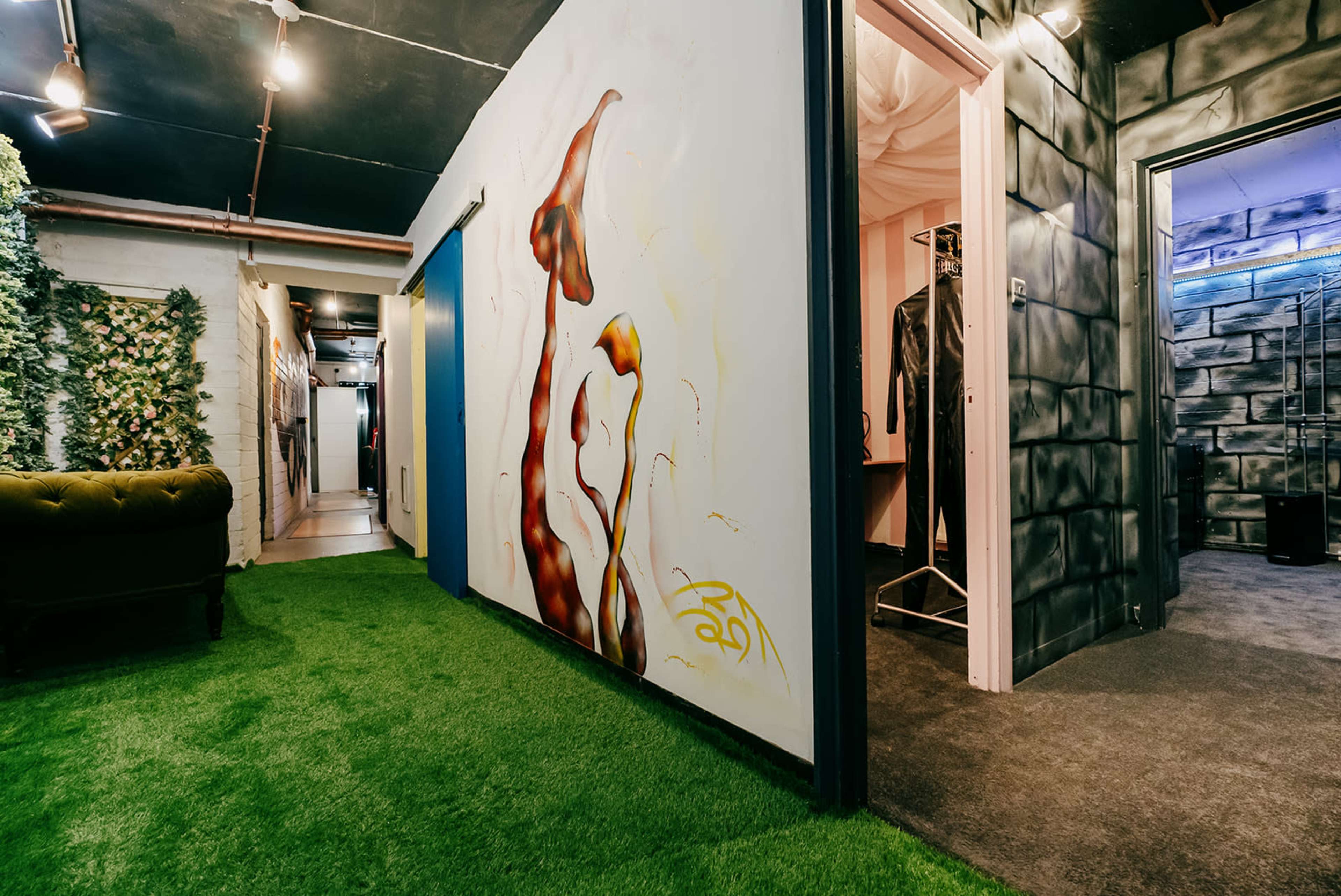 A hallway with green artificial grass flooring, a colorful mural on one wall, and various doorways leading to other rooms.