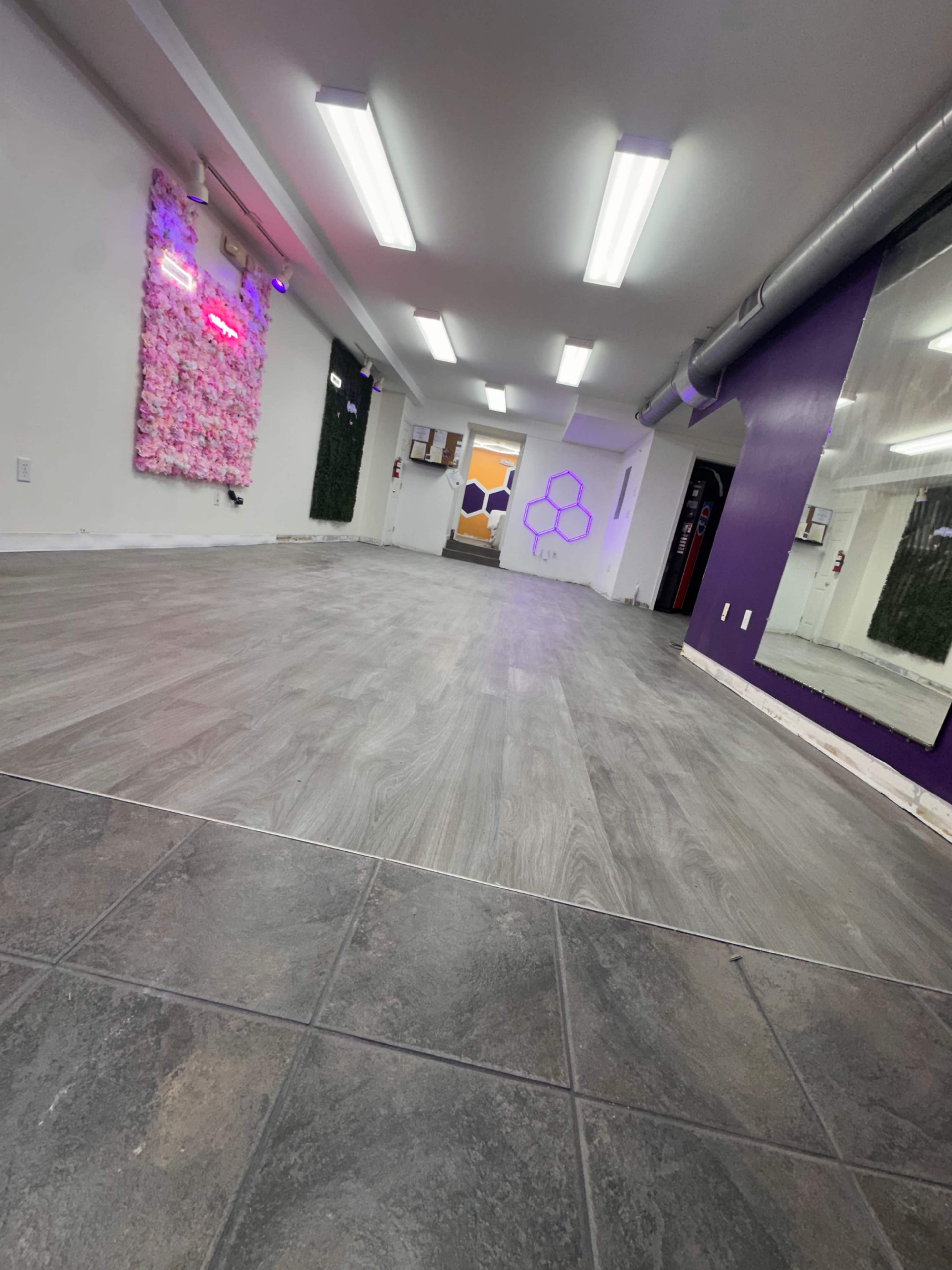 The image shows an empty interior space with gray laminate flooring and sections of purple and white walls.