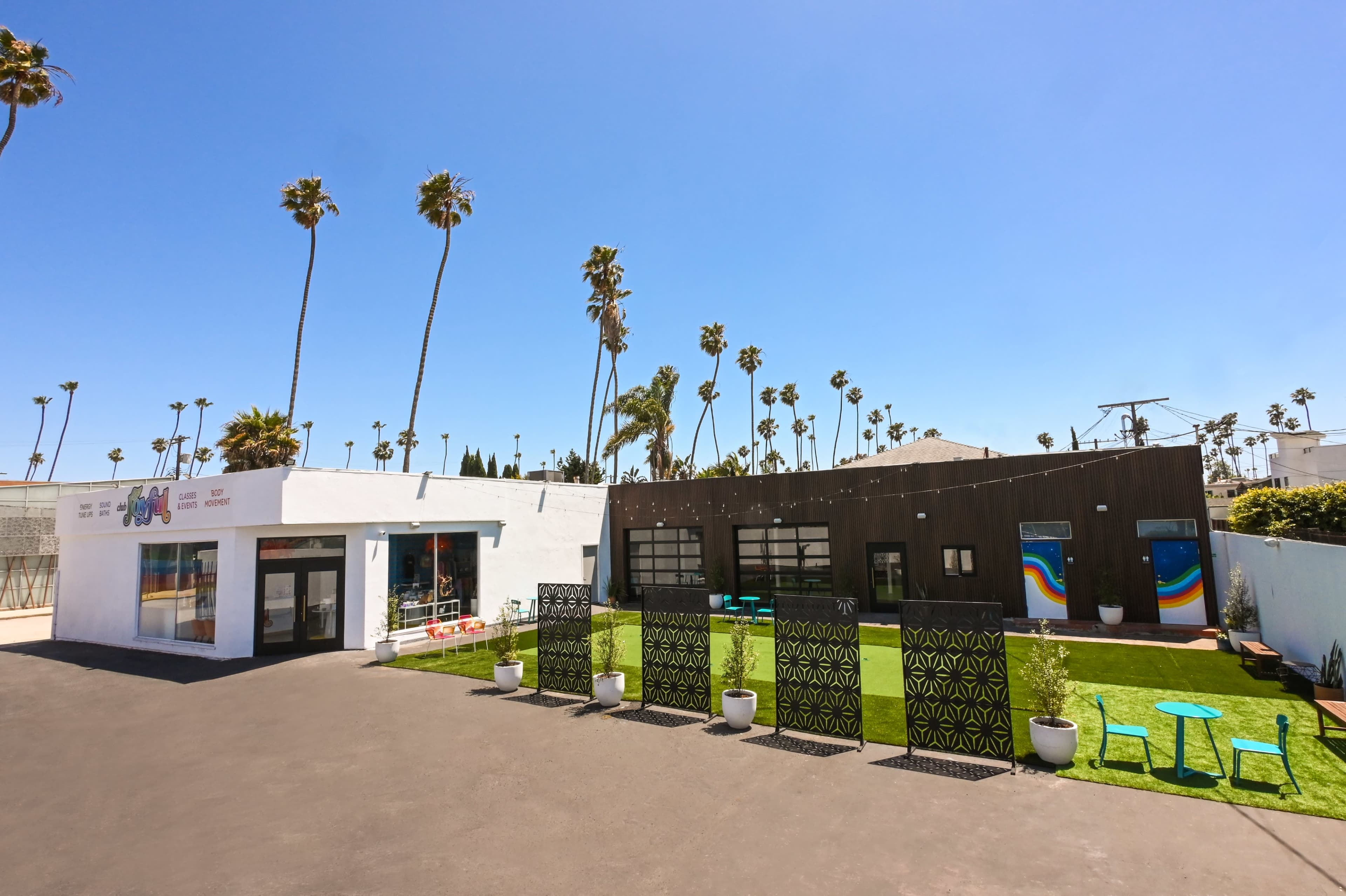A modern building with large windows, surrounded by palm trees and featuring a landscaped area with green grass and seating.