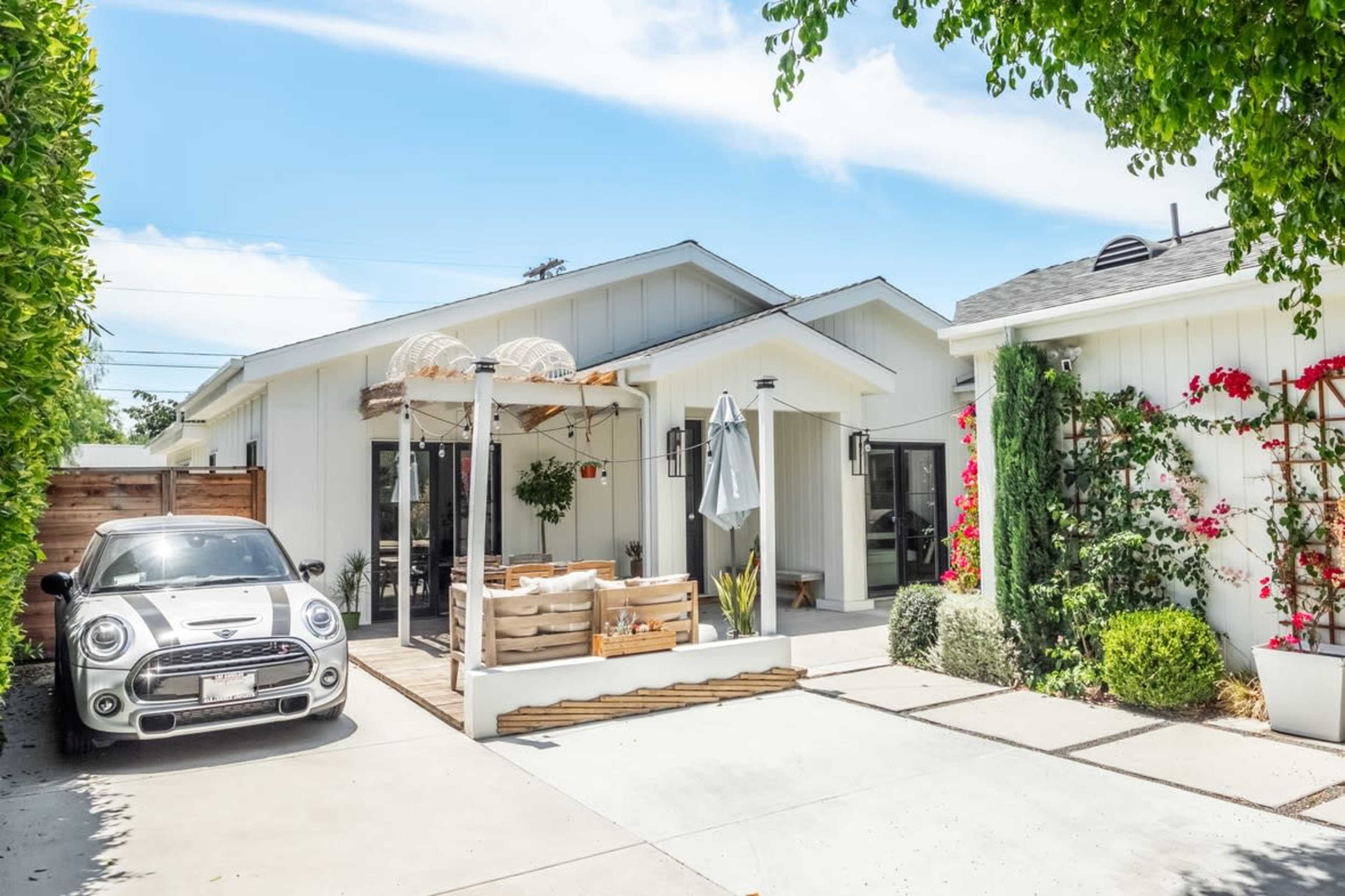 A modern house with a landscaped front yard, a parked car, and a patio area featuring outdoor furniture and plants.