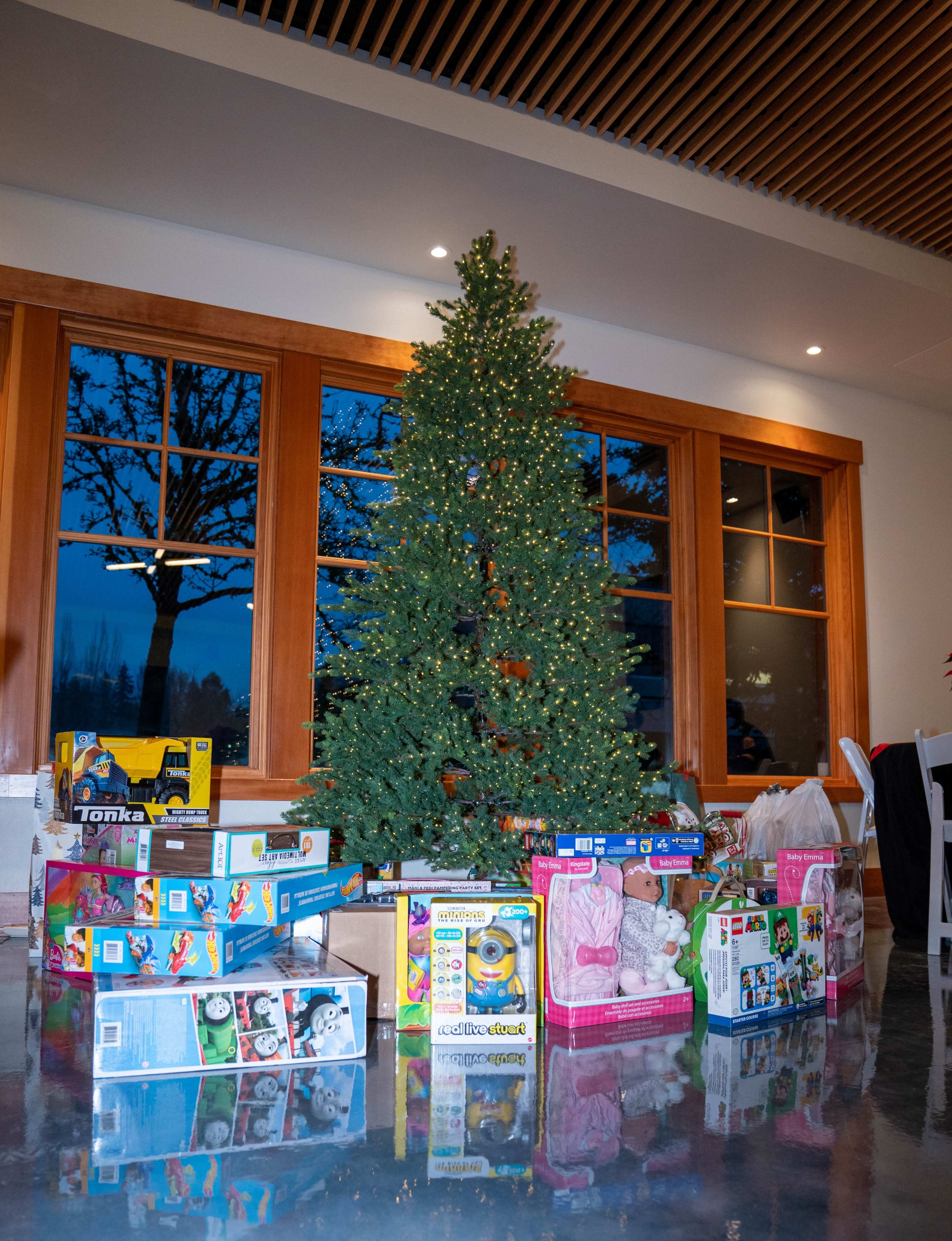 A decorated Christmas tree stands in a room surrounded by various unopened toy boxes.