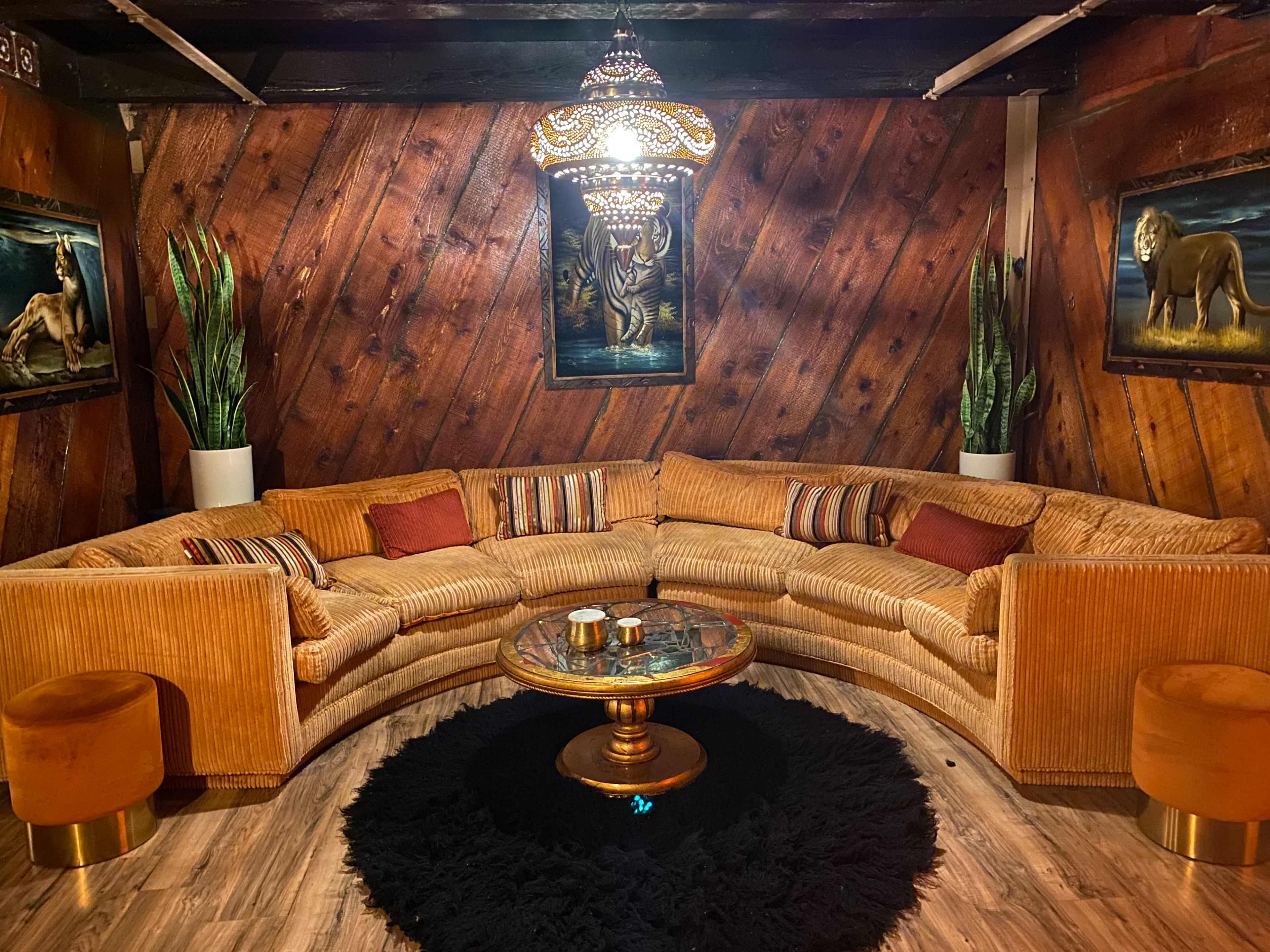 A spacious, circular sectional sofa is arranged around a glass coffee table on a black area rug, with potted plants and animal-themed artwork on the walls.