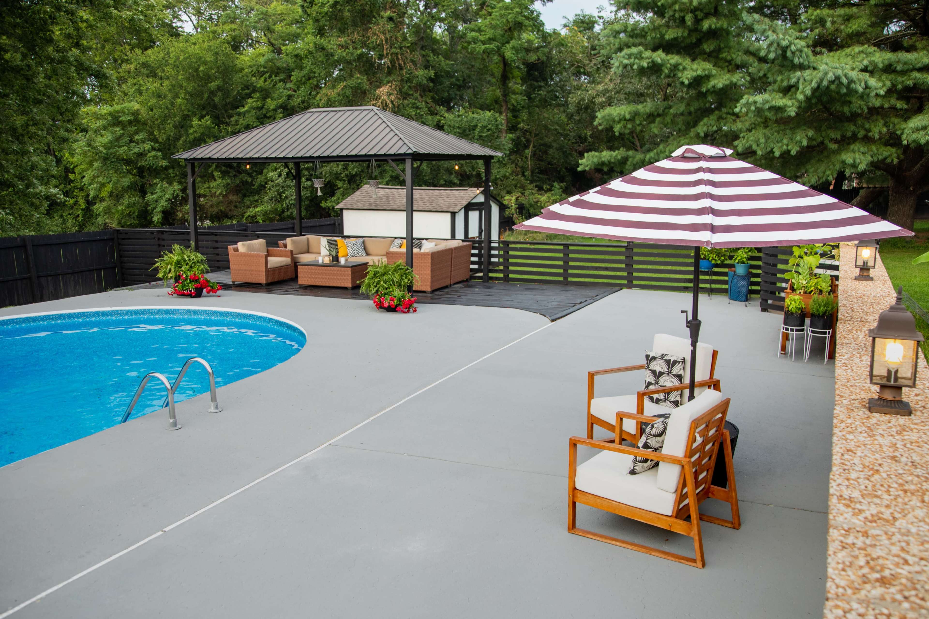 A spacious backyard features a swimming pool, a shaded seating area under a gazebo, and a striped umbrella beside a lounge chair.