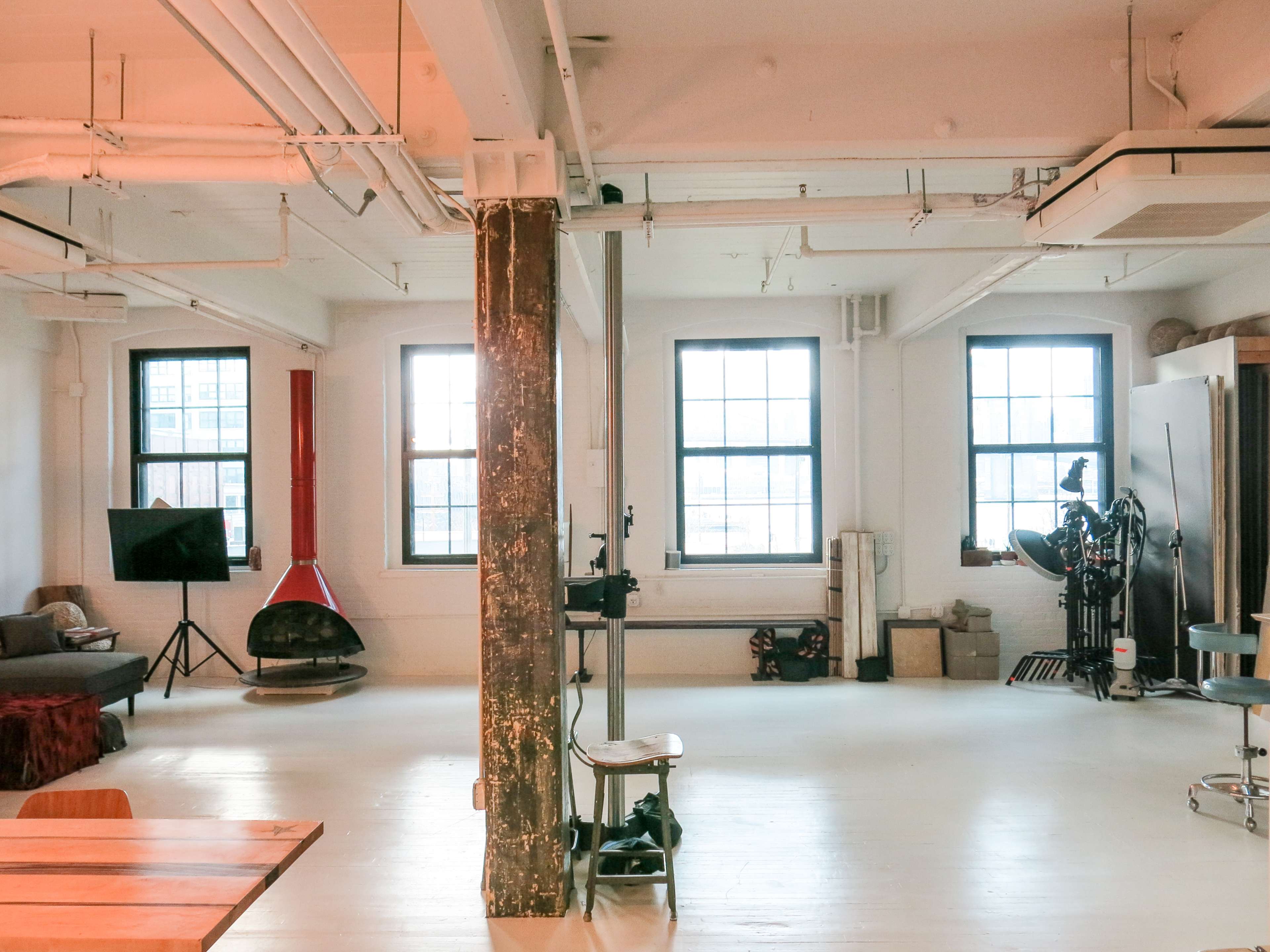 A spacious studio with large windows, wooden beams, and various furniture and equipment arranged throughout the room.