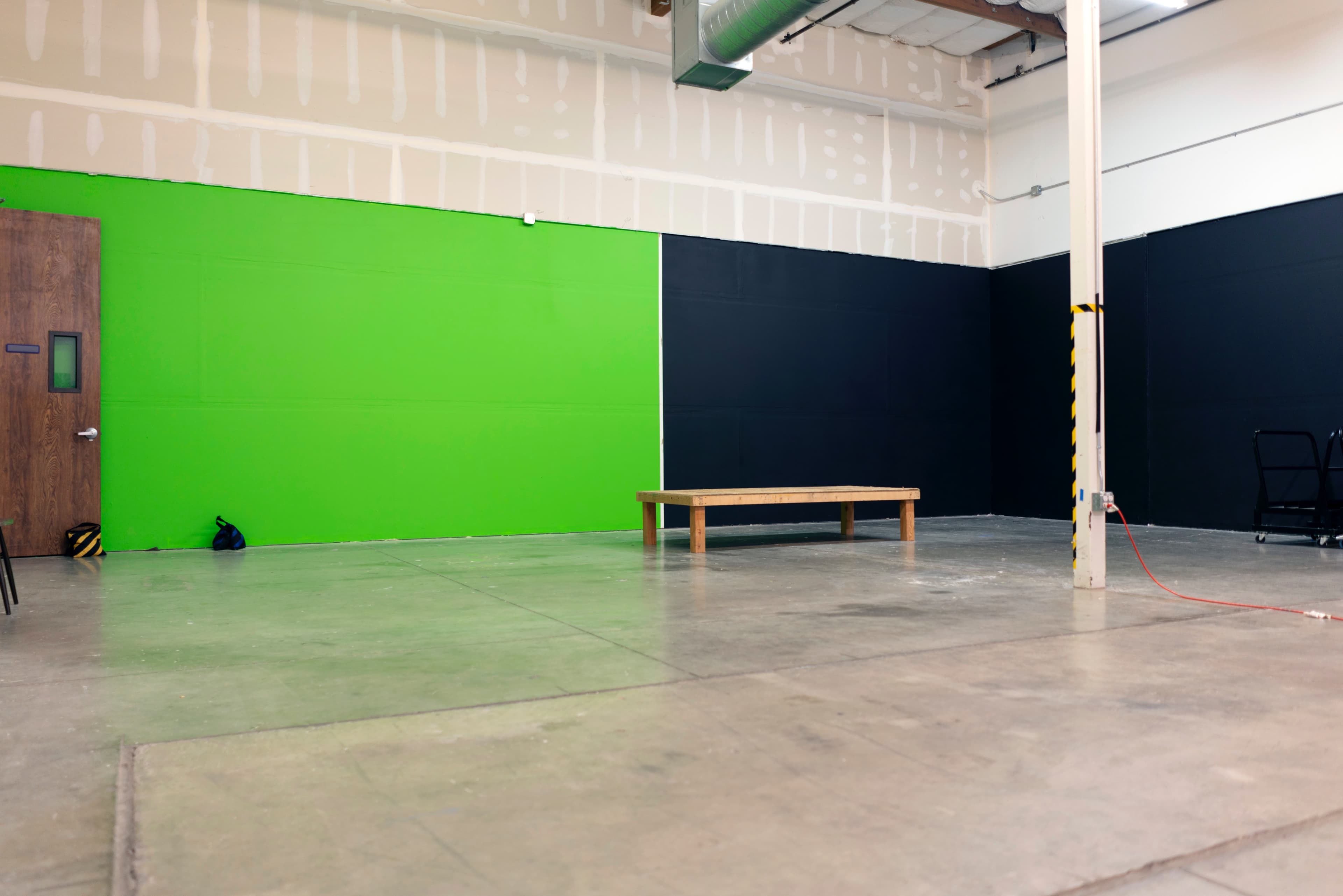 A spacious interior with a green wall, a black wall, a wooden table in the center, and a concrete floor.