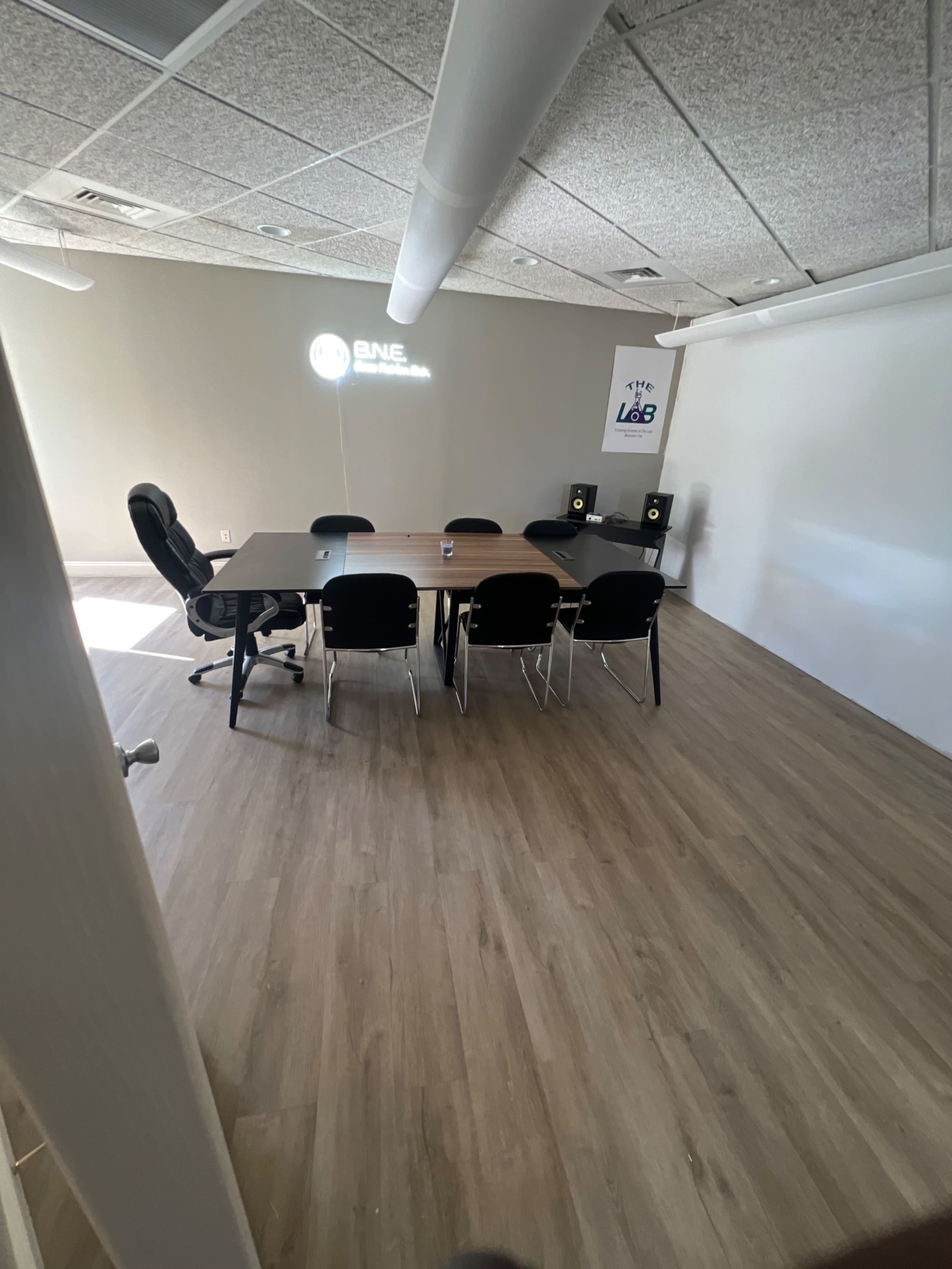 A conference room with a large table surrounded by black chairs, a swivel chair in the corner, and projectors mounted on the walls.