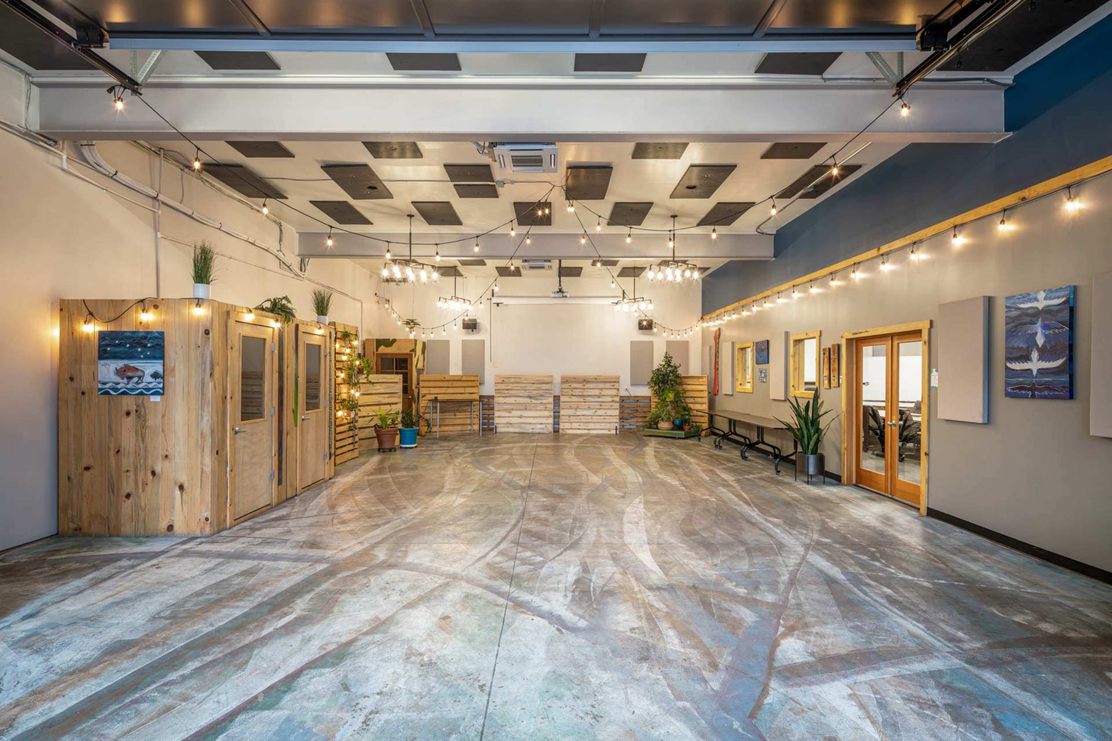 The image shows a spacious indoor venue with a polished concrete floor, wooden features, hanging lights, and decorative plants.