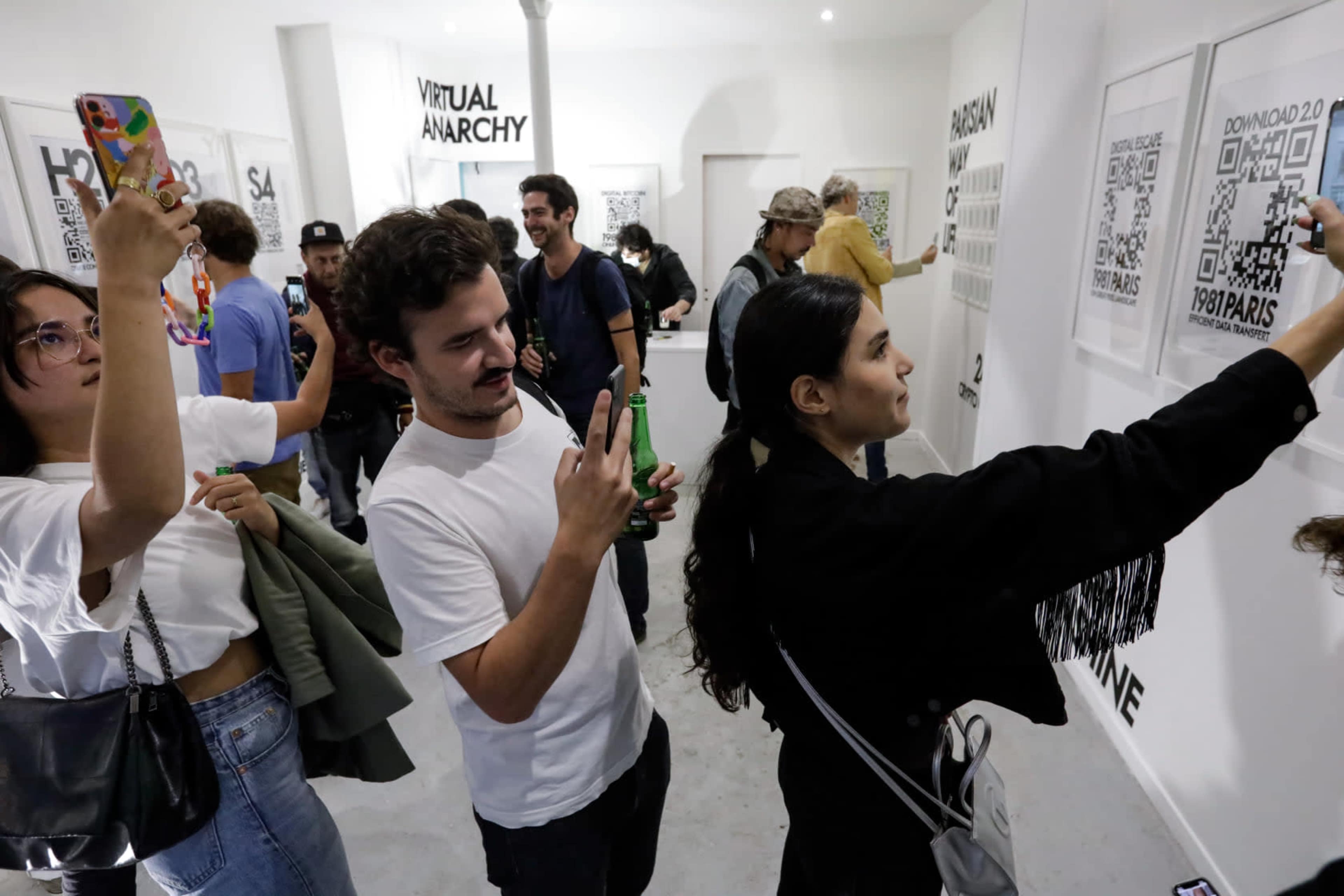 A group of people are interacting with artwork on the walls of an exhibition, with some taking photos and others viewing QR codes.