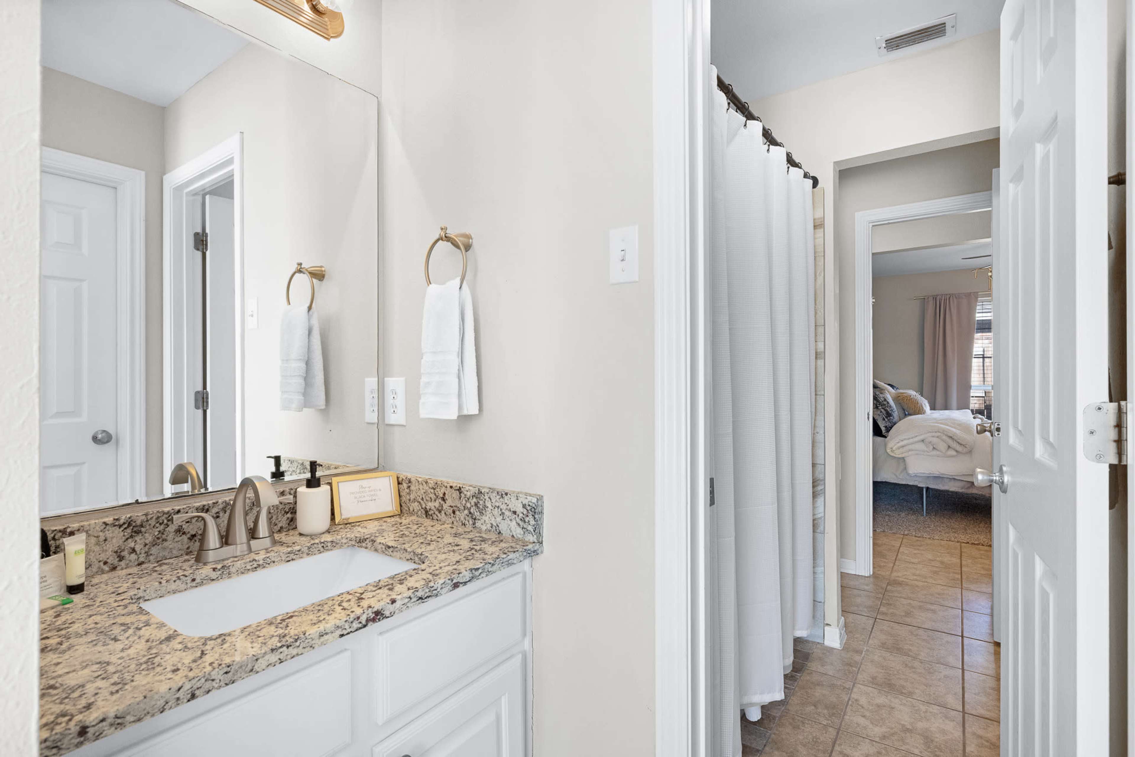The image features a modern bathroom with a granite countertop sink, a mirror, and a shower curtain, leading to a room beyond.