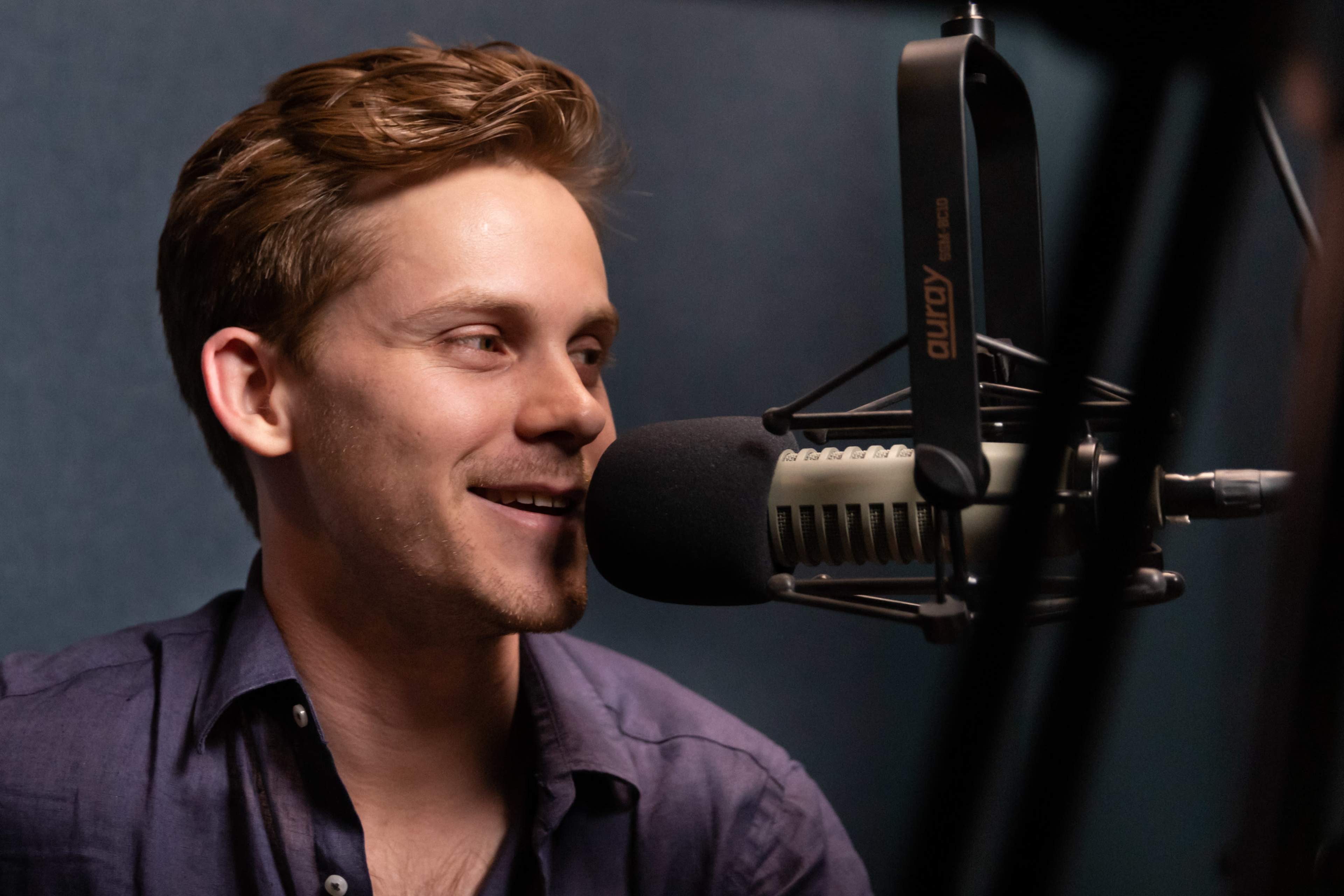 A man is sitting in front of a microphone, smiling as he engages in conversation.