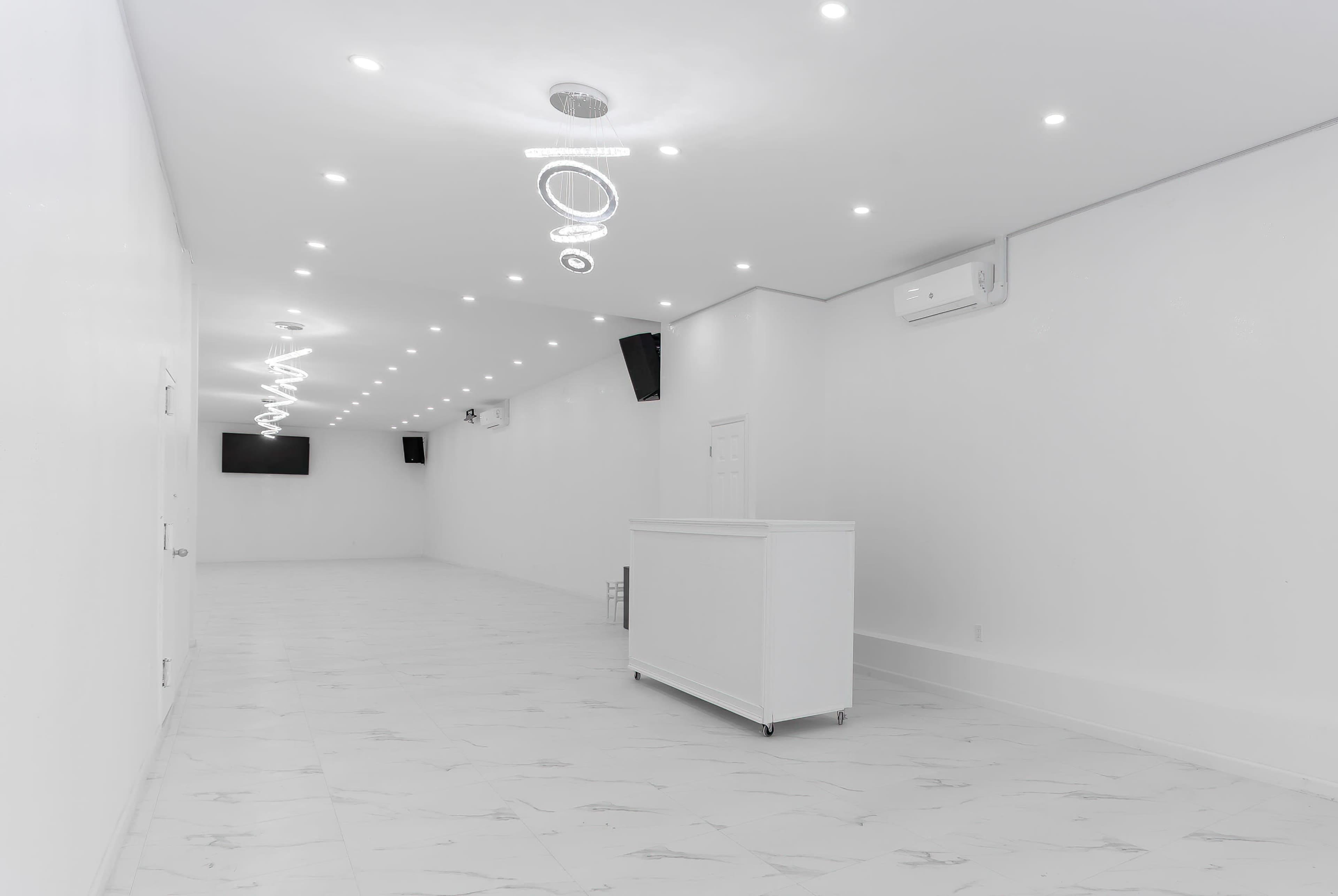 A large, empty room with white walls, bright ceiling lights, and a reception area featuring a white counter.