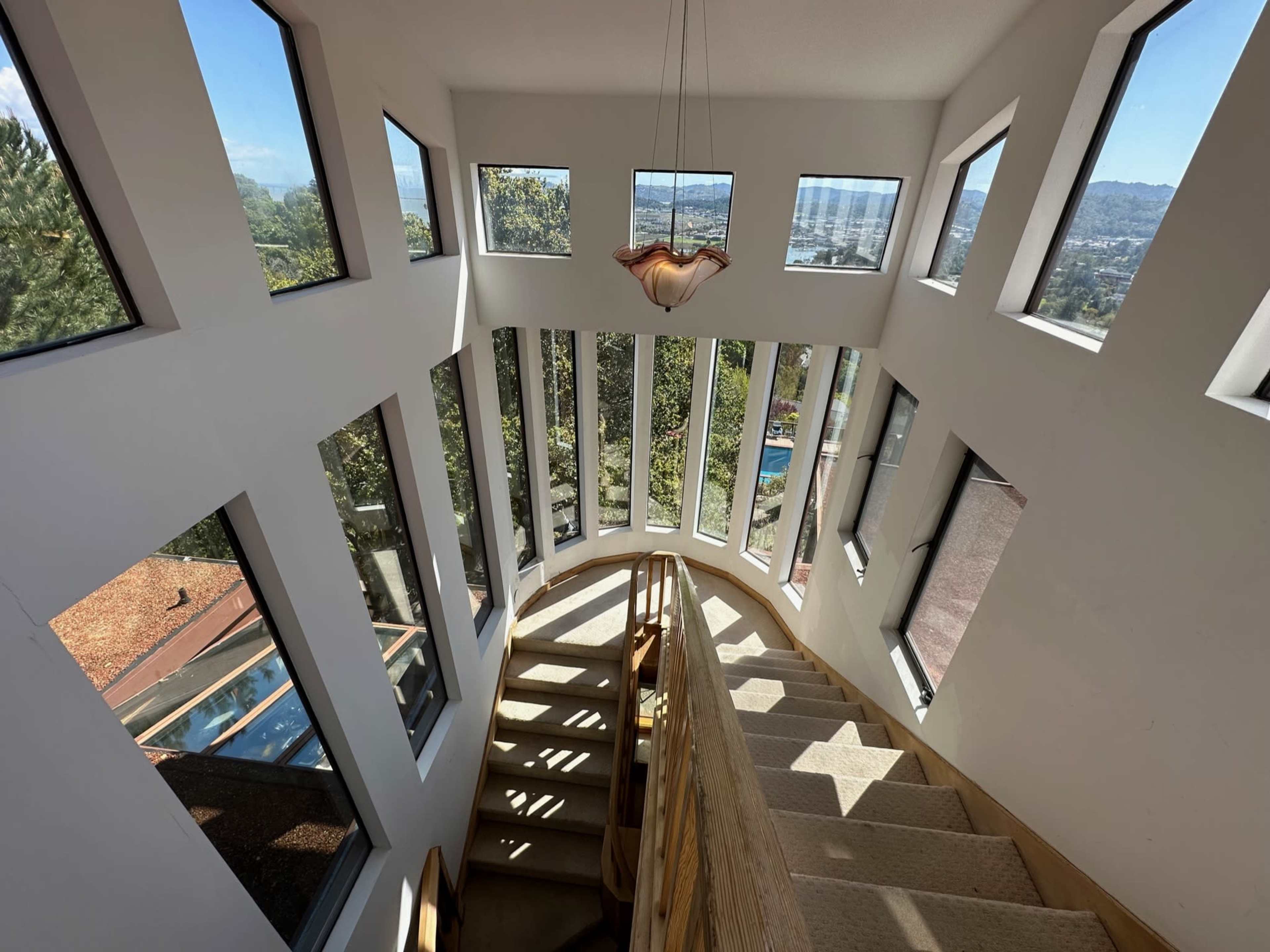 The image shows a spiral staircase leading down in a modern building with large windows that offer views of the surrounding landscape.