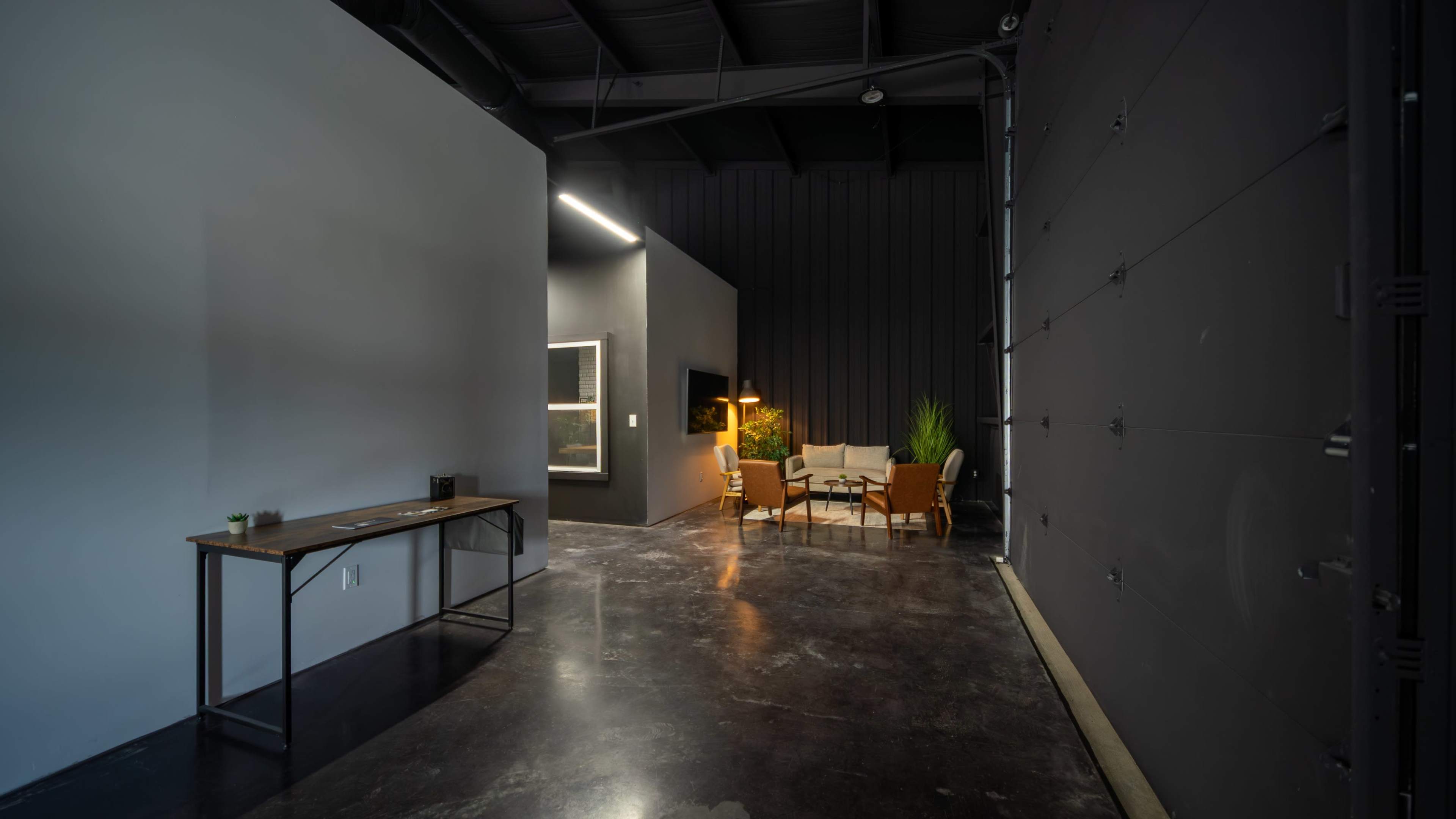 The image shows a modern, open interior space with a polished concrete floor, featuring a waiting area with seating and a side table.